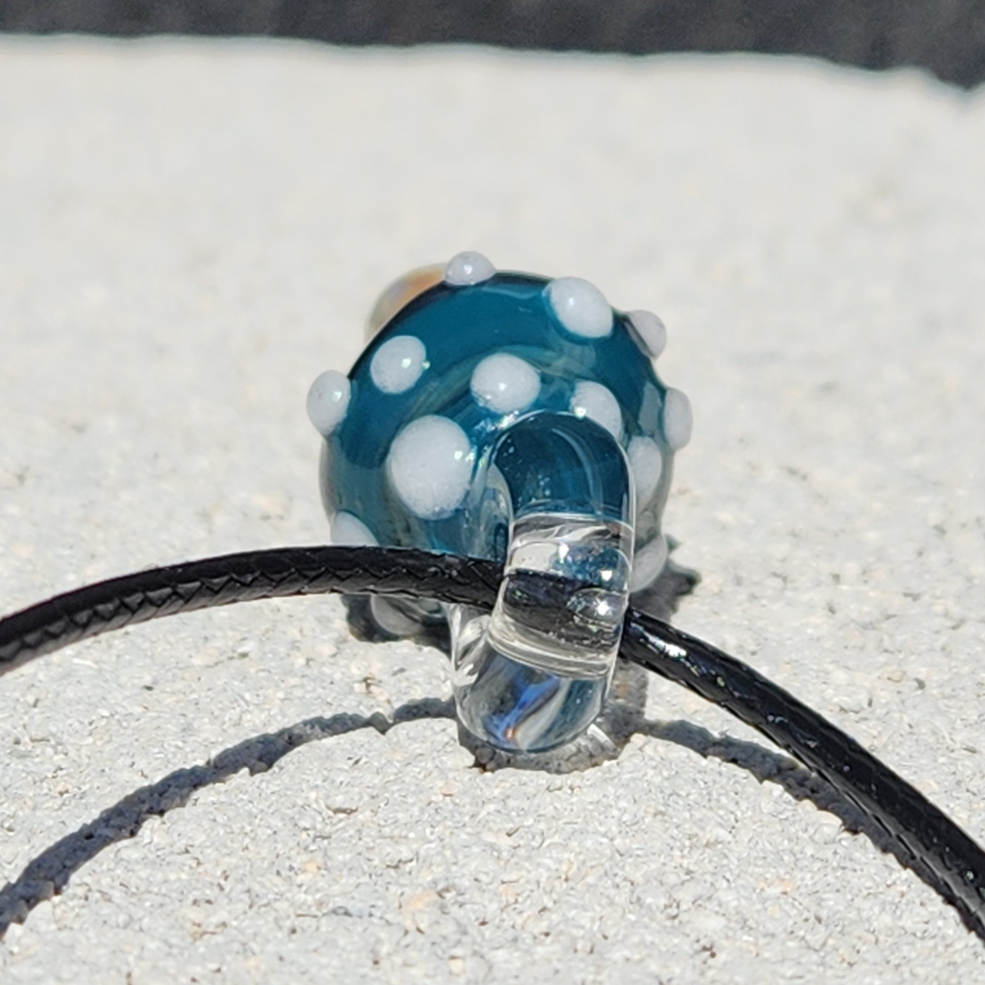 Close-up of Blue Mushroom Art Glass Pendant showing detailed white spots and clear loop on black cord. Unique handmade necklace for art lovers.