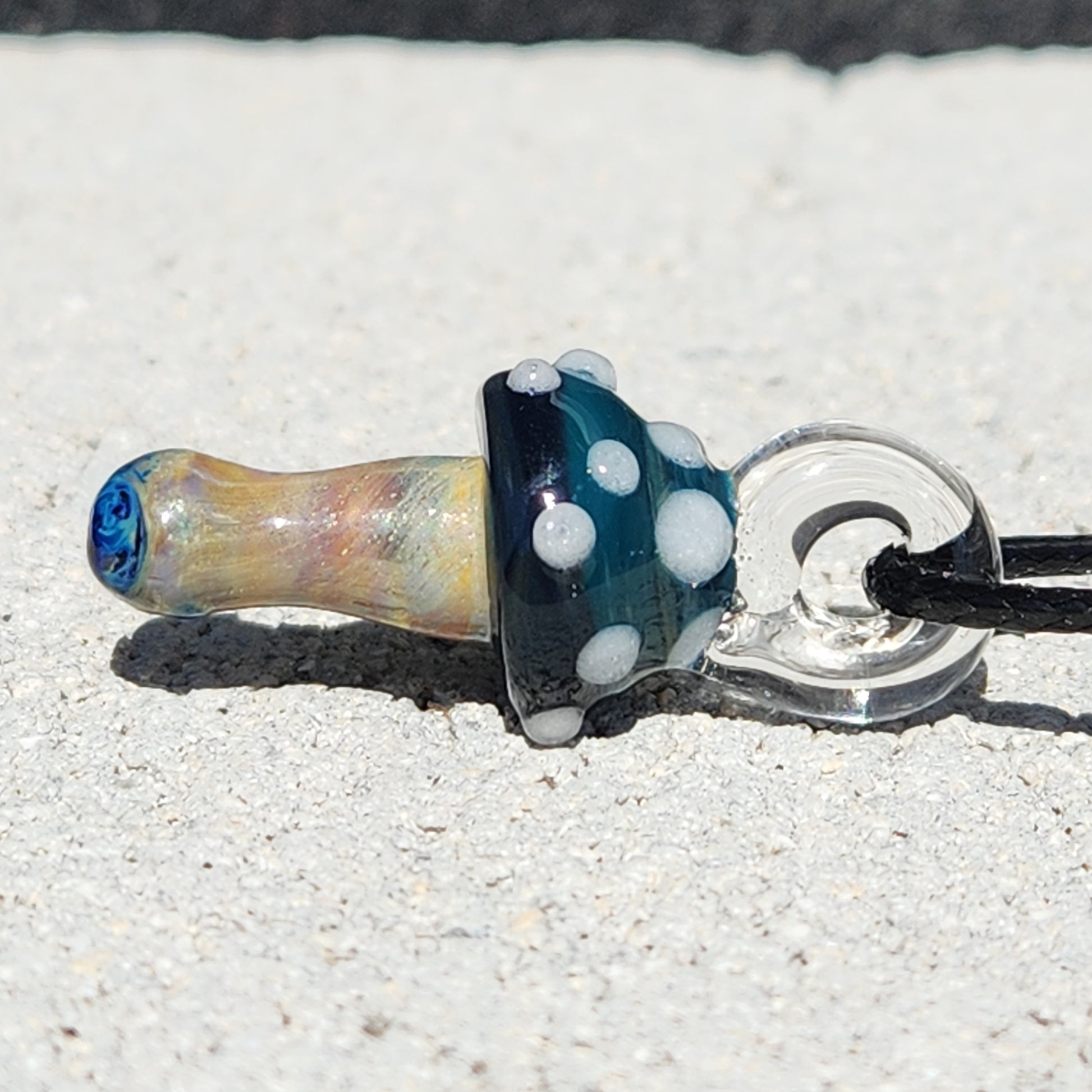 Side profile of Blue Mushroom Art Glass Pendant with clear loop and detailed cap. A small, handmade necklace for whimsical fashion lovers.