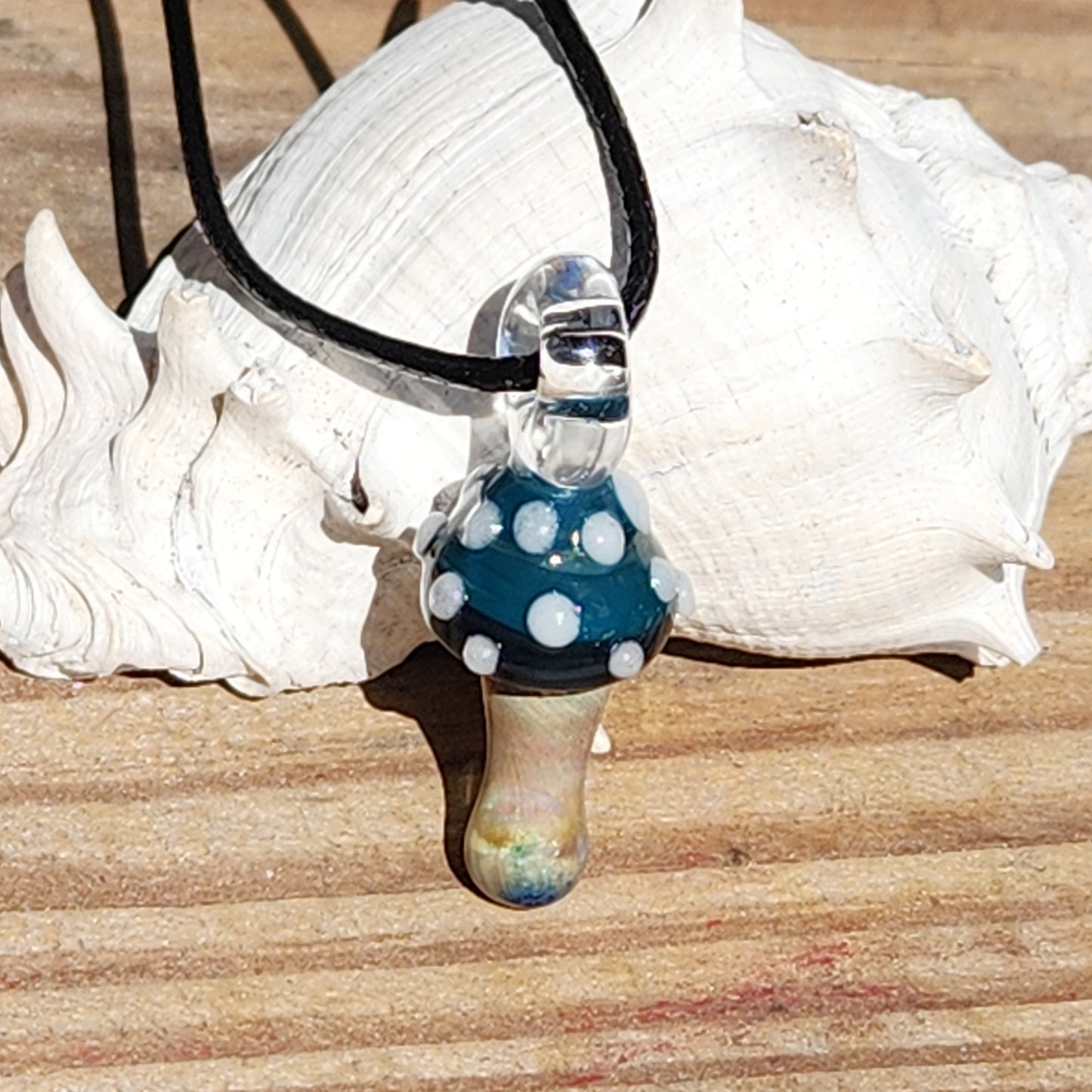 Blue Mushroom Art Glass Pendant resting on wood, showcasing its detailed craftsmanship and vibrant colors. A unique handmade necklace gift.