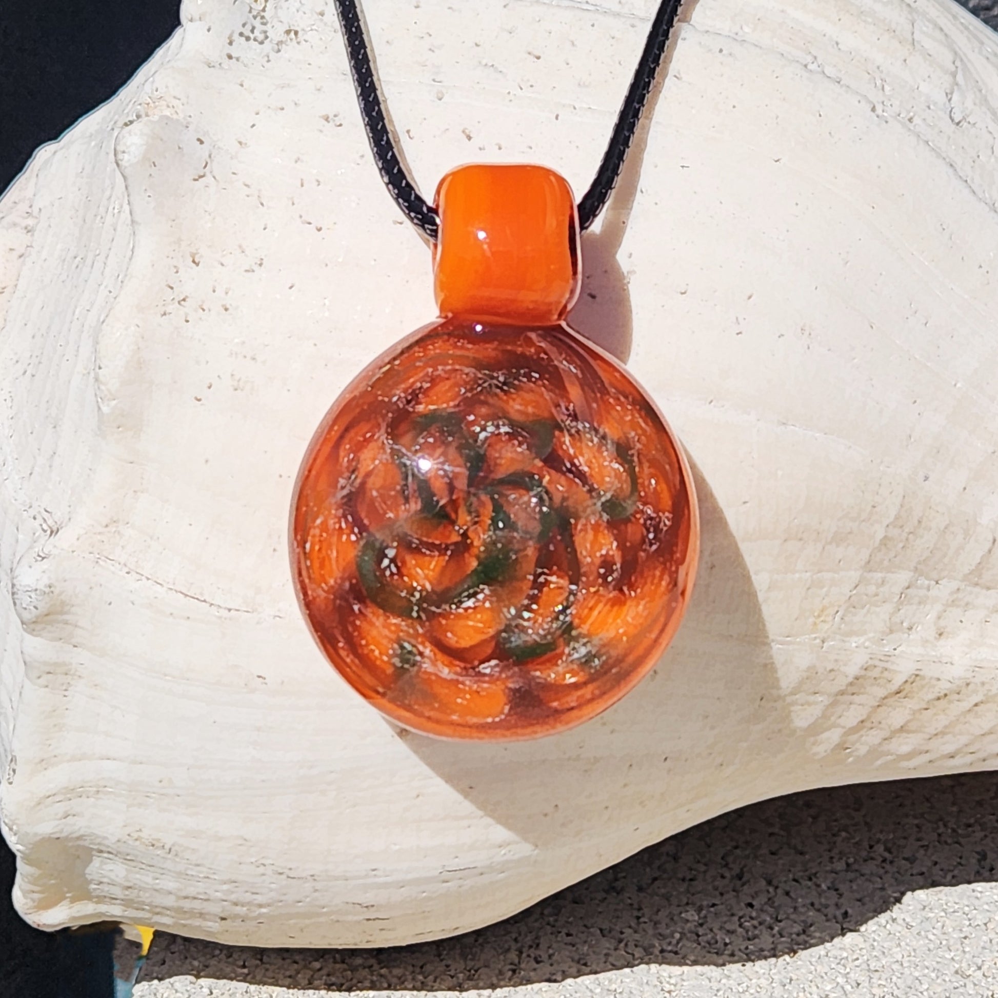 Handmade orange swirl dichroic glass pendant necklace with green and silver accents, displayed on a white seashell background.