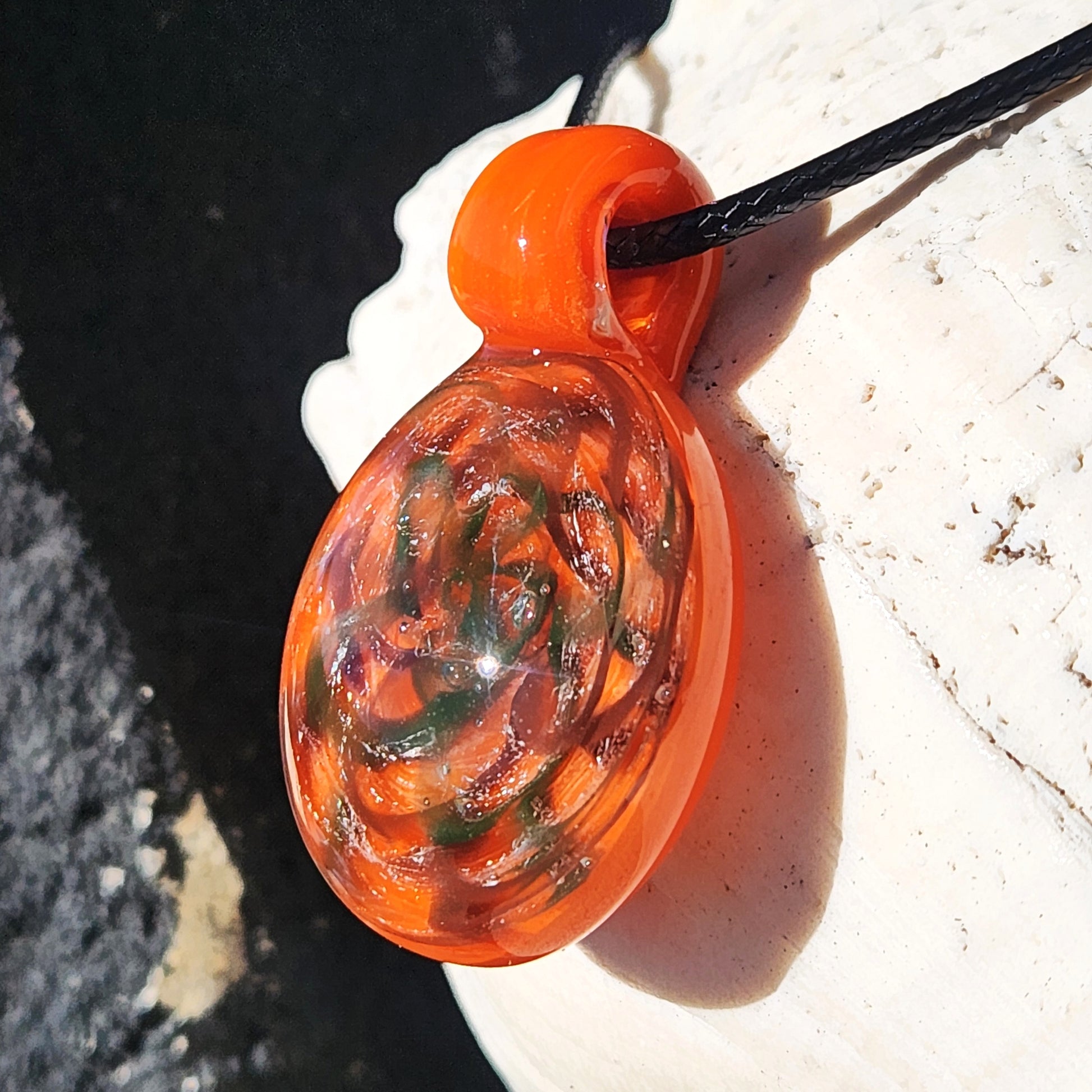 Close-up of heady glass pendant necklace with orange, green, and silver swirls, highlighting its glossy handmade finish.