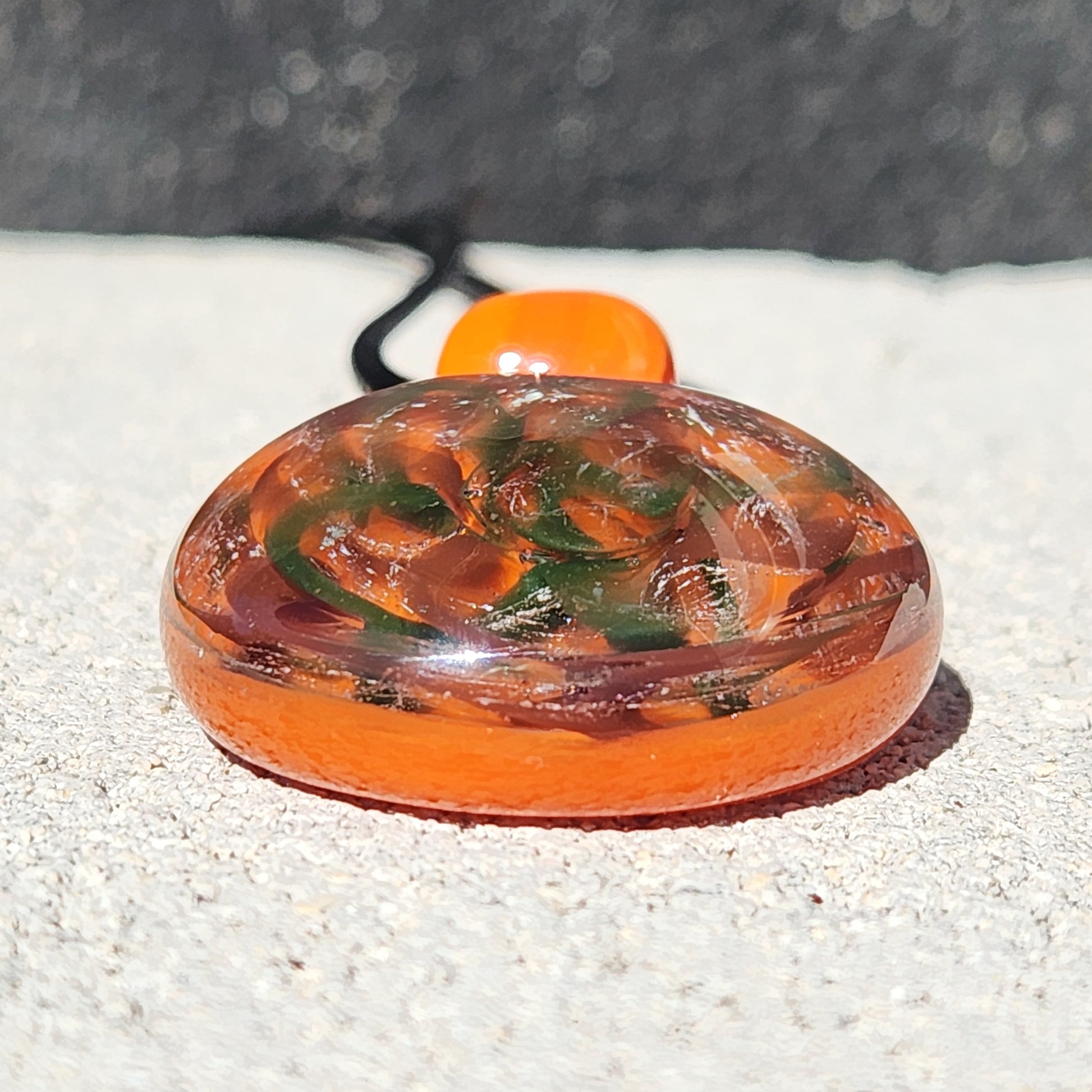 Low-angle view of dichroic glass pendant necklace showing its thick, rounded shape and vibrant orange and green swirls.
