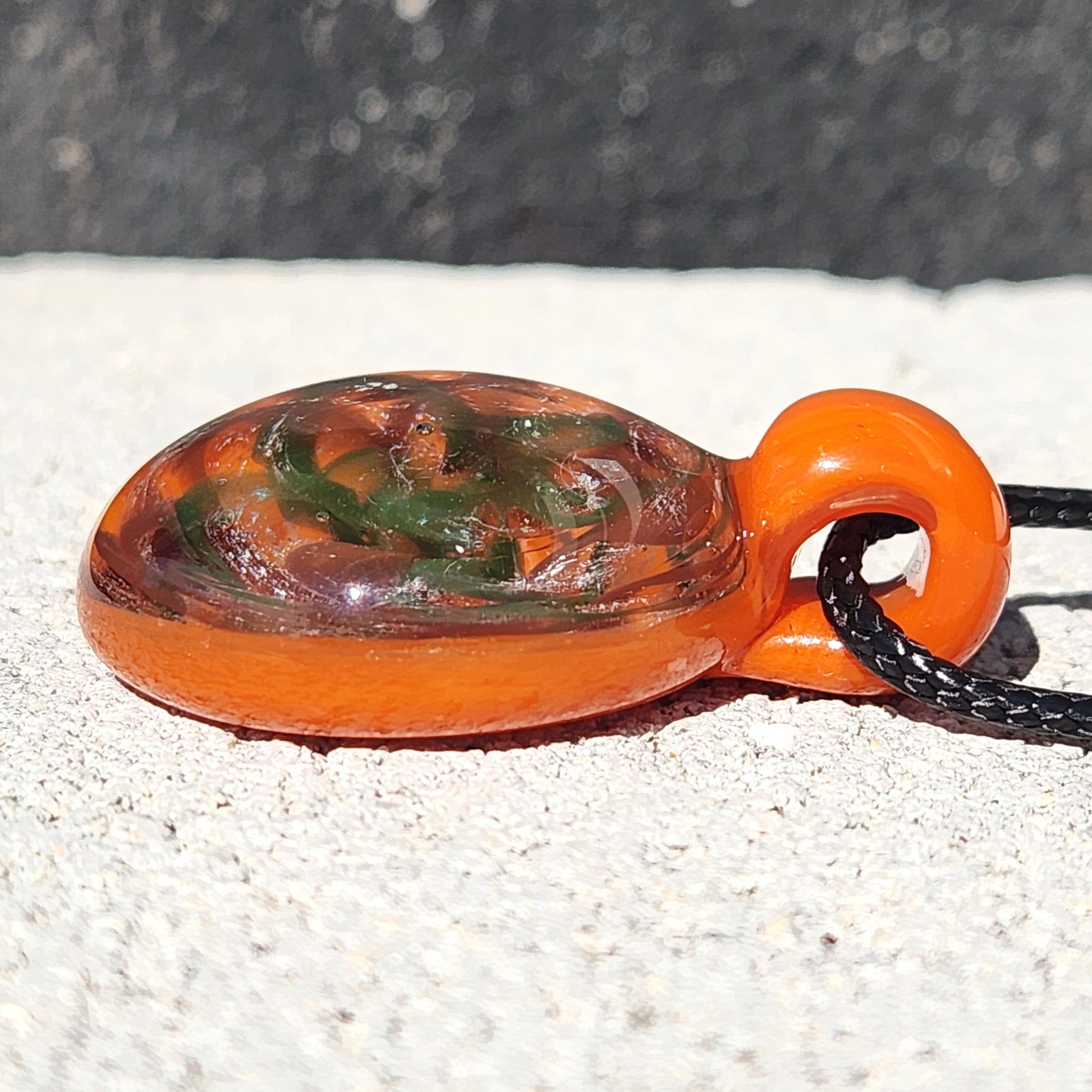 Side profile of orange swirl glass pendant necklace with black cord, showcasing its layered handmade glass design.