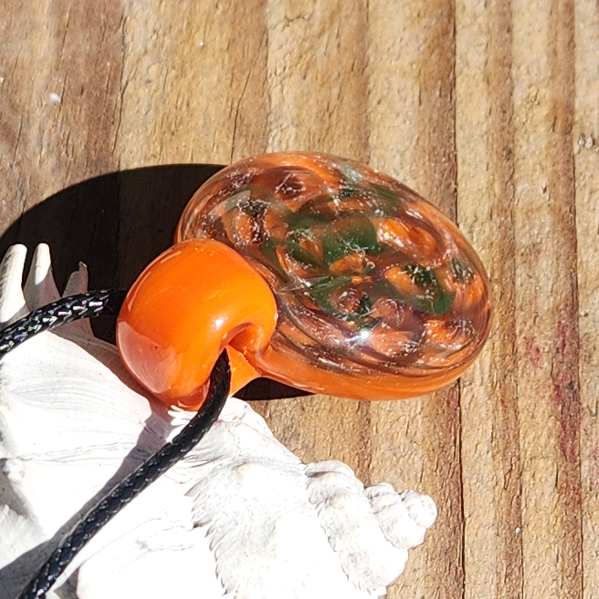 Side view of handmade orange glass pendant necklace showing its domed shape and intricate swirling green and silver details.