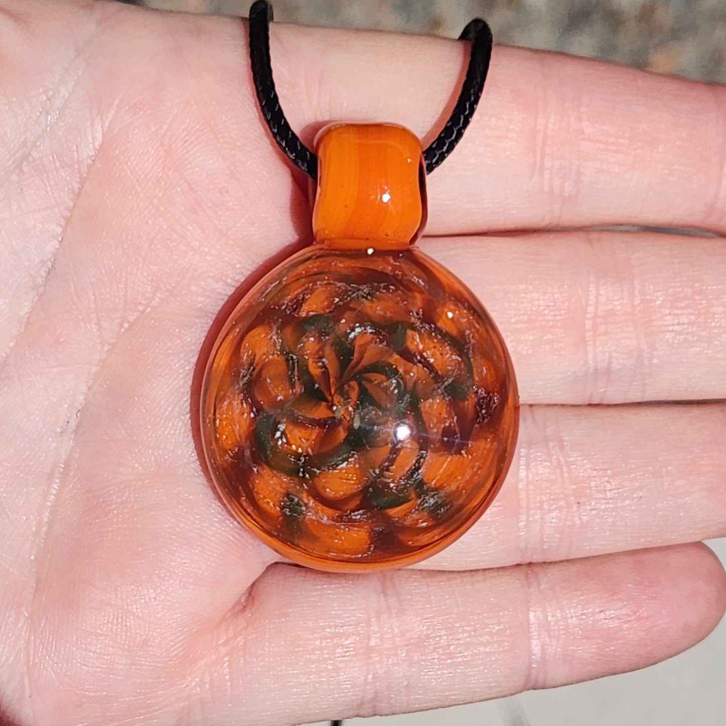 Hand holding handmade orange swirl glass pendant necklace, highlighting its size and intricate swirling design.