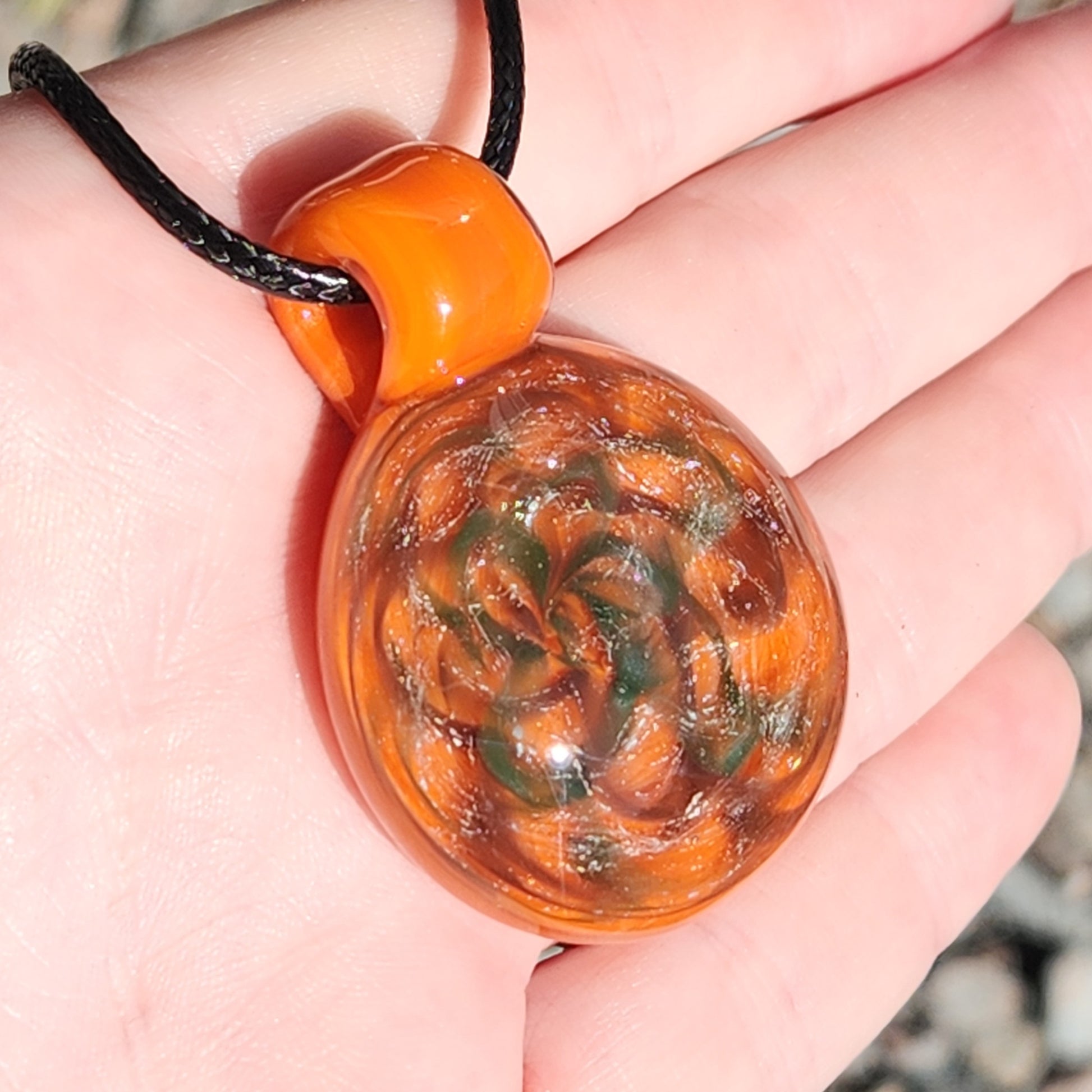 Brightly lit view of orange dichroic glass pendant necklace in hand, showing green and silver swirl details up close.