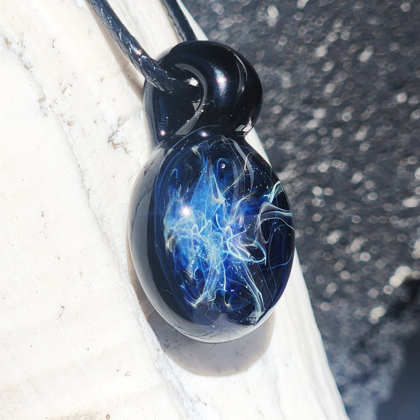 Artisan glass pendant with glowing blue and silver swirls, photographed on a white shell to highlight its handcrafted detail.