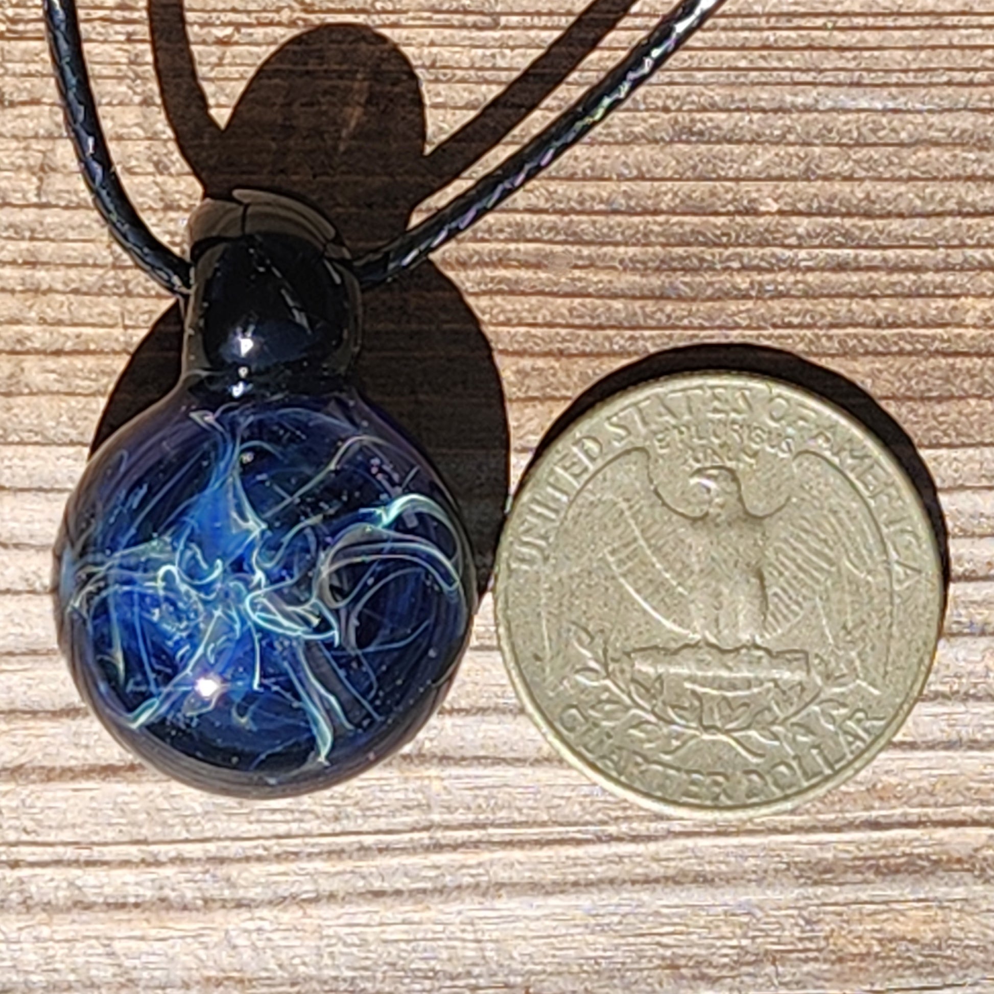 Size comparison of small blue swirl glass pendant necklace next to a US quarter, highlighting its compact handmade design.