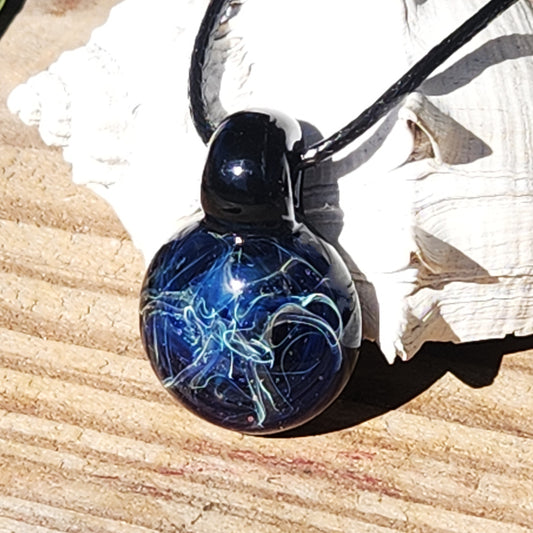 Handmade blown glass pendant necklace with blue and silver swirl design, shown on a wooden surface with seashell background.
