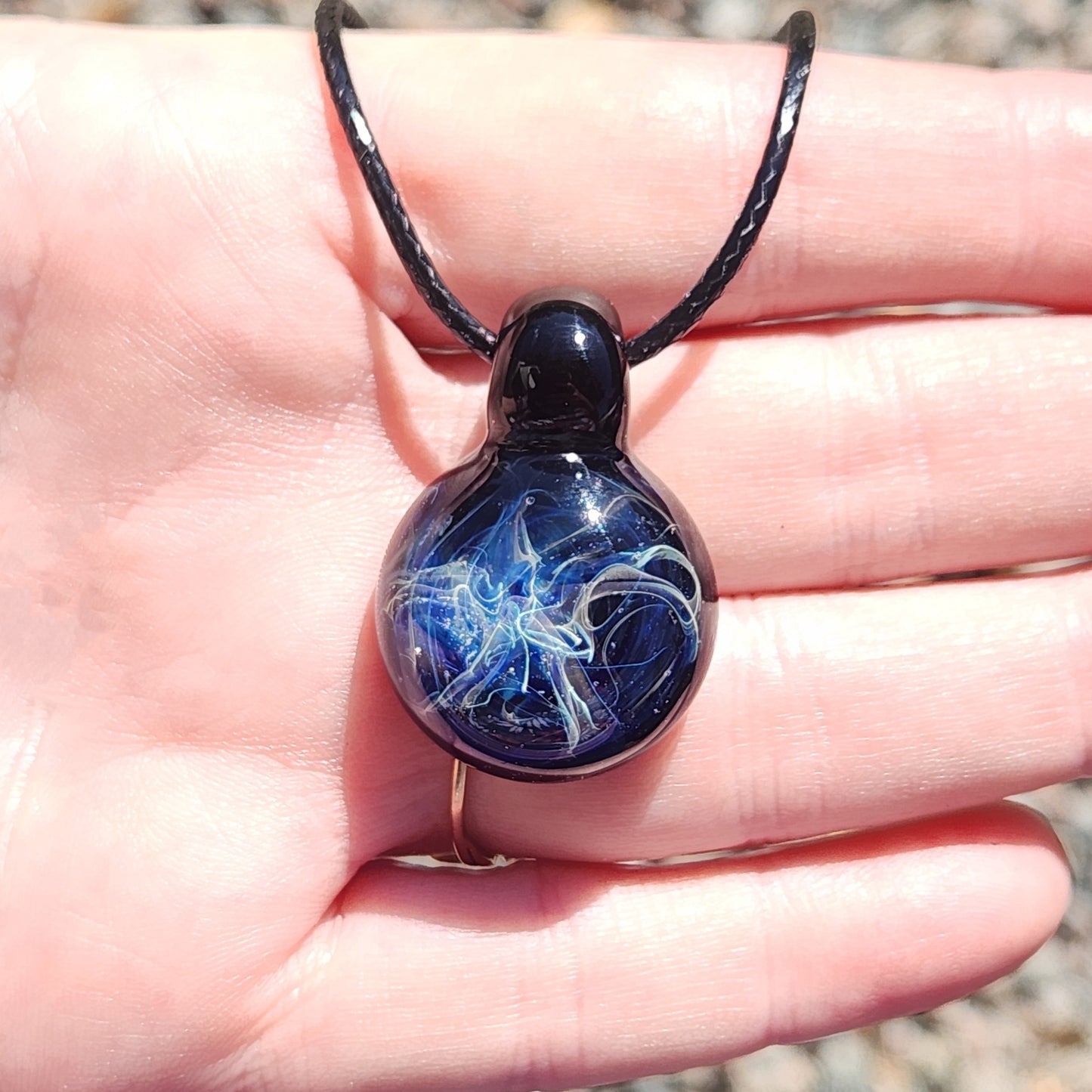 Hand holding a handmade blown glass pendant necklace with vivid blue and silver swirls, ideal as a unique birthday gift.