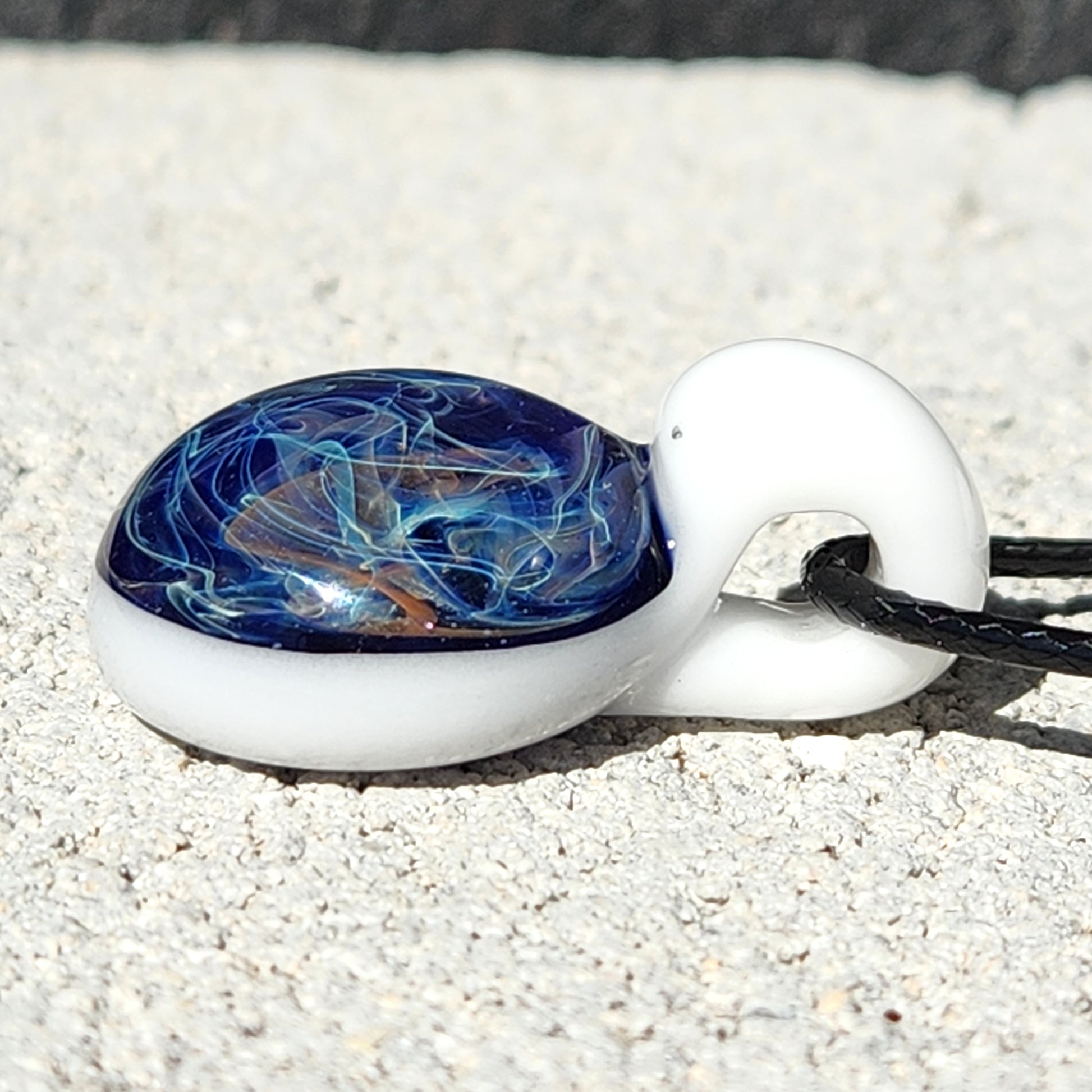 Detailed view of Deep Blue Galaxy Pendant Necklace lying on sand, showcasing its handmade glass craftsmanship and cosmic design.