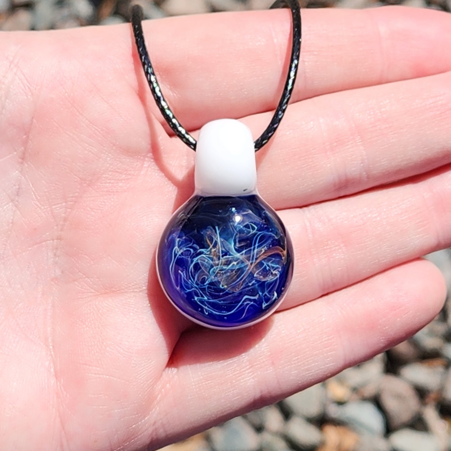 Deep Blue Galaxy Pendant Necklace held in hand, highlighting its small size and intricate handmade glass detailing.