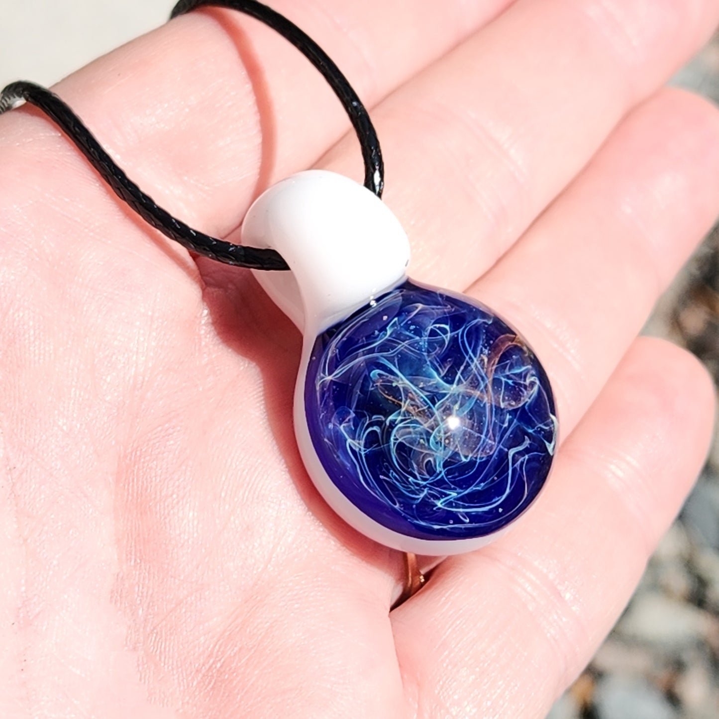 Close-up of Deep Blue Galaxy Pendant Necklace in palm, showcasing swirling blue, white, and gold design in artisan glass jewelry.