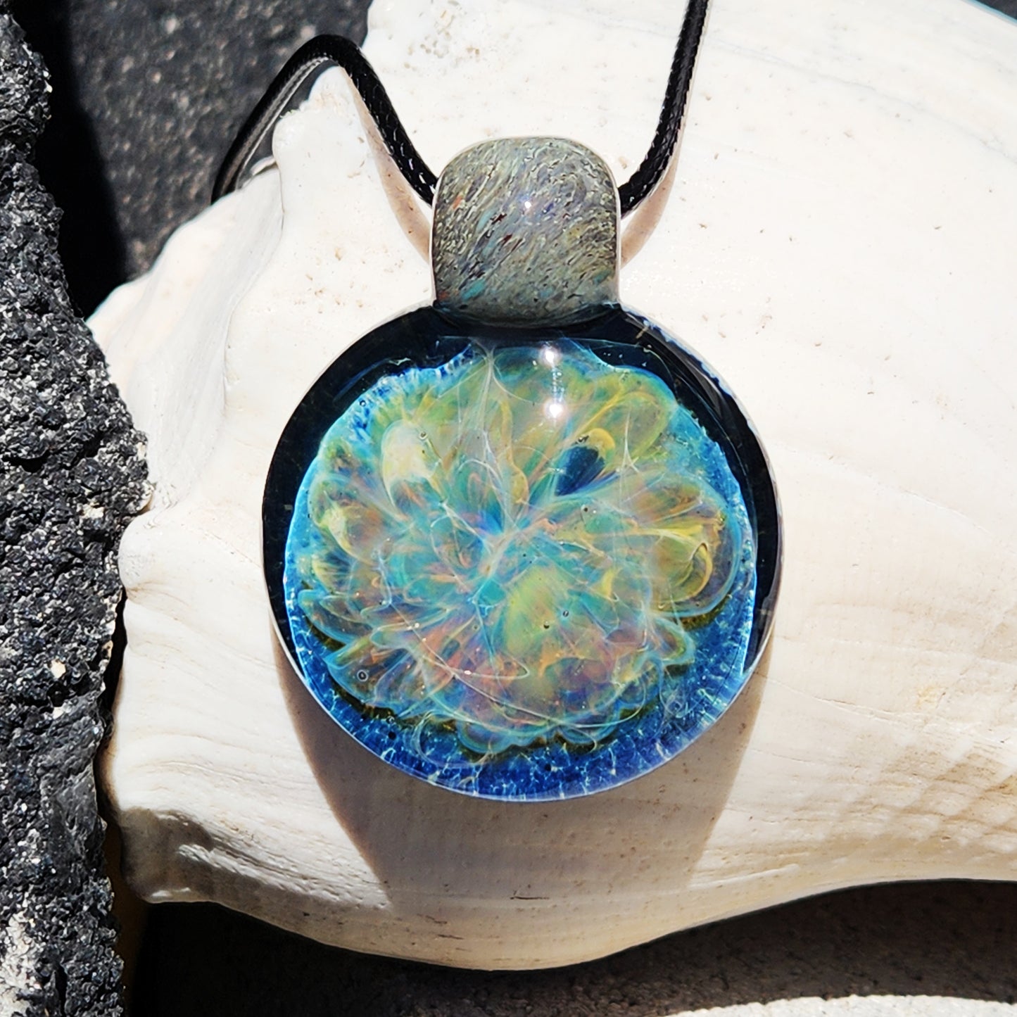 Handmade Glass Pendant Necklace with swirling blue and iridescent colors, displayed on a seashell. Unique one-of-a-kind jewelry gift.
