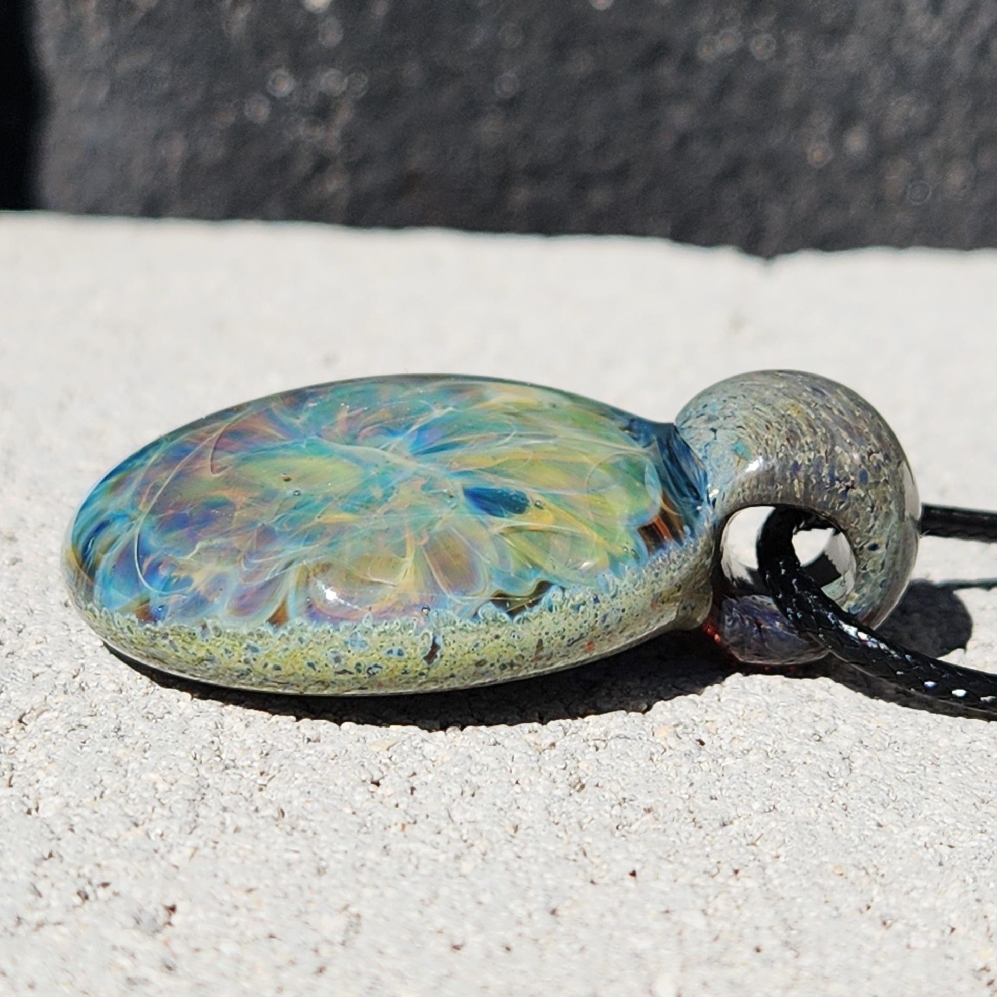 Side view of Handmade Glass Pendant Necklace showing its domed shape and colorful wave-like interior. Unique glass jewelry design.
