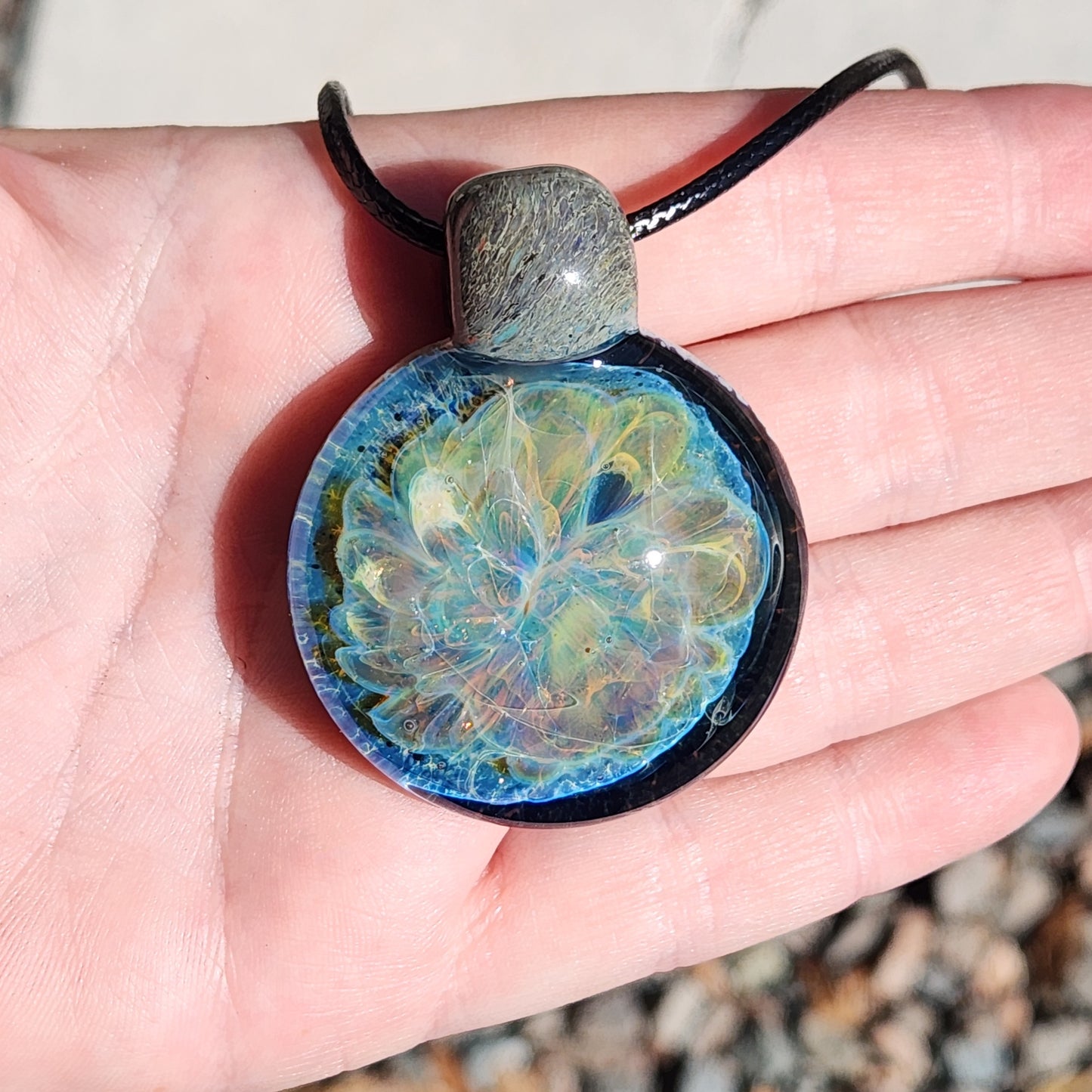 Stormy Ocean Waves Glass Pendant Necklace resting in hand, showcasing its vivid blue and iridescent glasswork. Handmade and gift-ready.