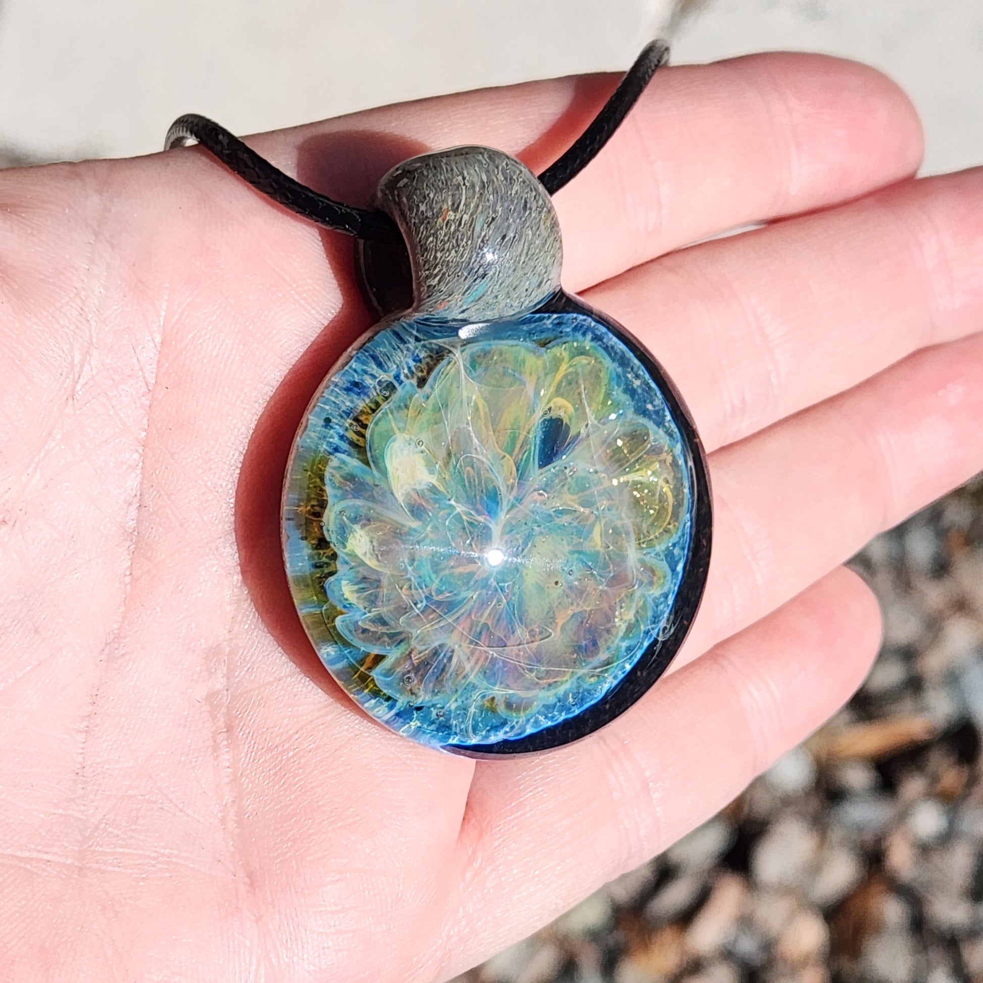 Stormy Ocean Waves Glass Pendant Necklace shown in hand, highlighting its vibrant blue and silver iridescent design. Handmade glass jewelry.