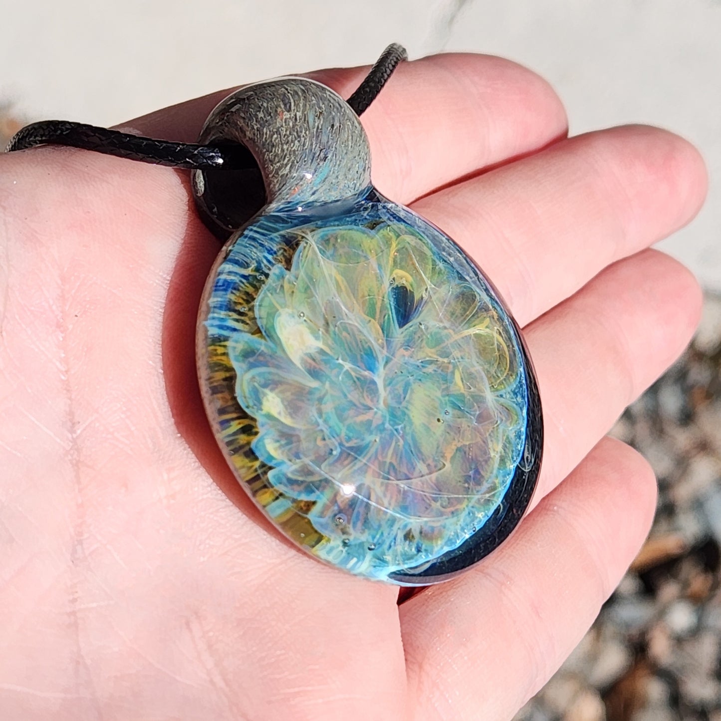 Angled view of Handmade Glass Pendant Necklace in hand, emphasizing its swirling ocean-inspired colors and glossy finish. Unique jewelry piece.