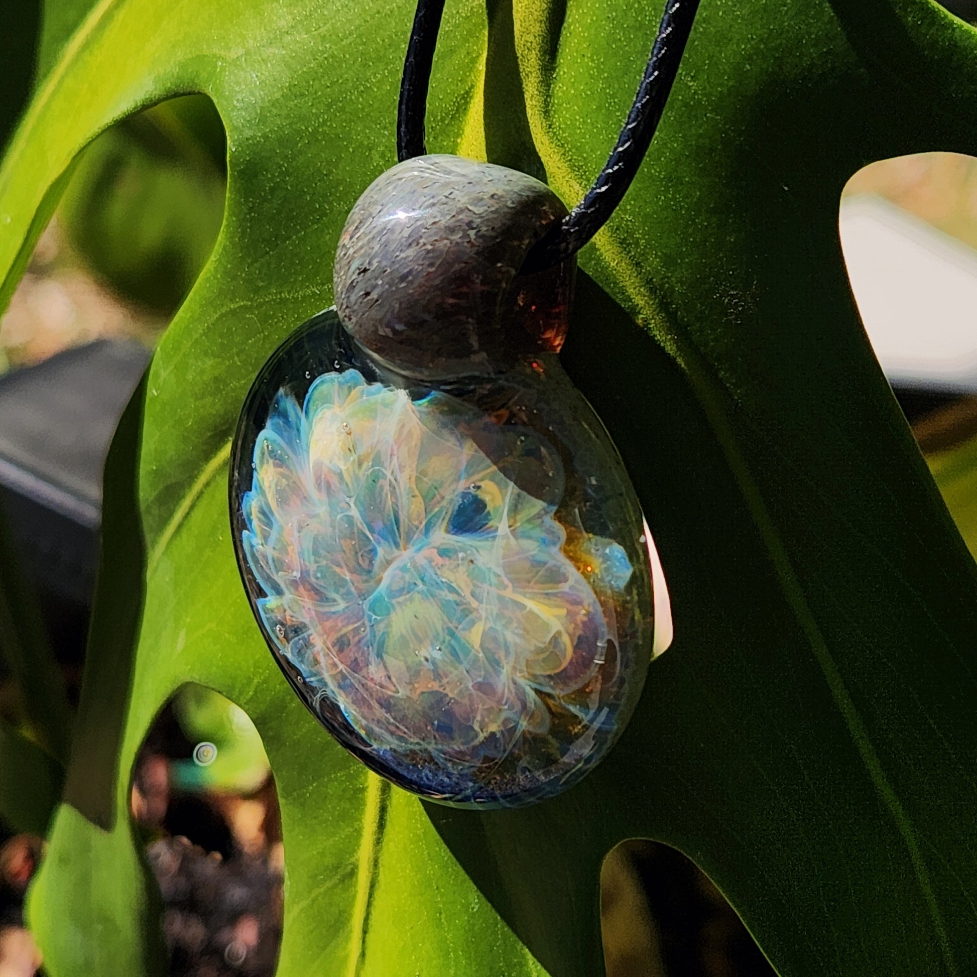 Unique Handmade Glass Pendant Necklace featuring ocean-inspired swirls, hanging against a green leaf. One-of-a-kind glass jewelry piece.