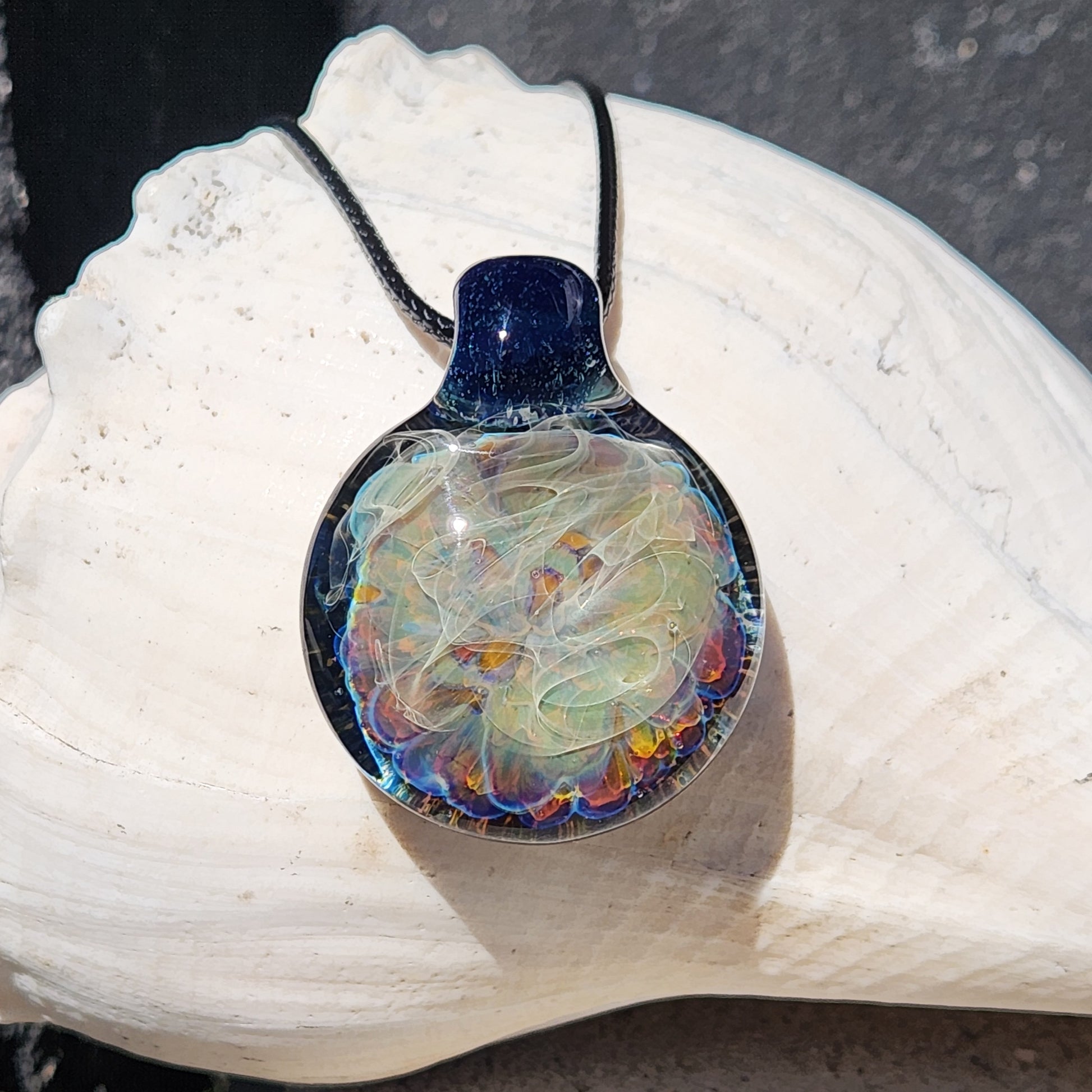 Unique handmade glass pendant necklace featuring colorful borosilicate layers and silver fuming, shown on a white seashell background.
