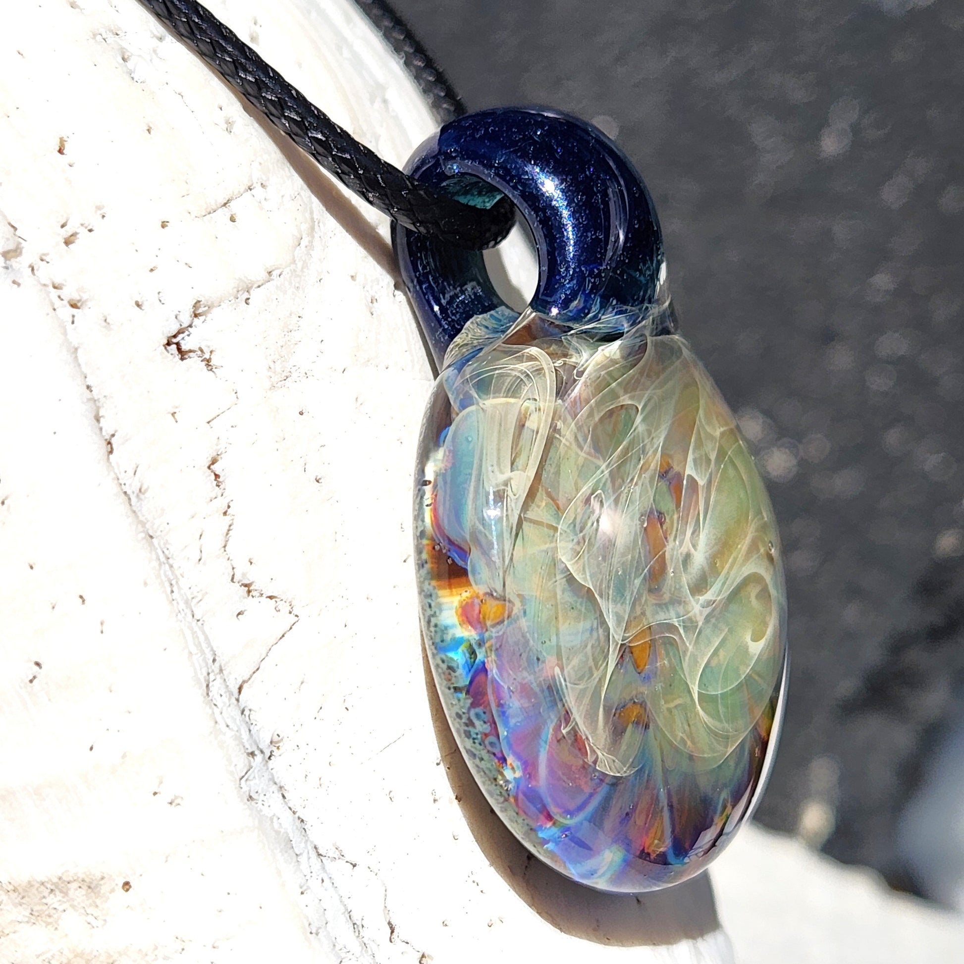 Side view of handmade blown glass pendant necklace with iridescent colors and smooth finish, highlighting its artistic craftsmanship.