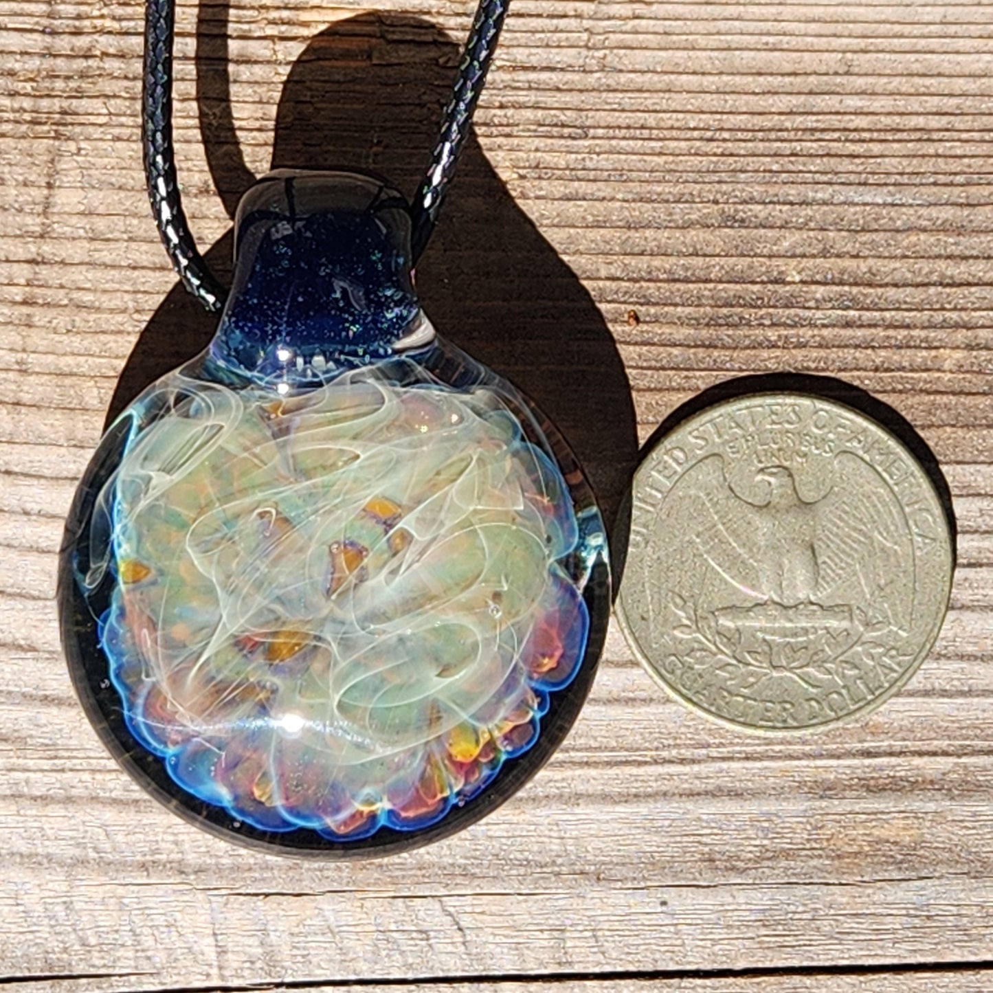 Handmade blown glass pendant necklace next to a US quarter for size comparison, featuring colorful swirls and silver accents.