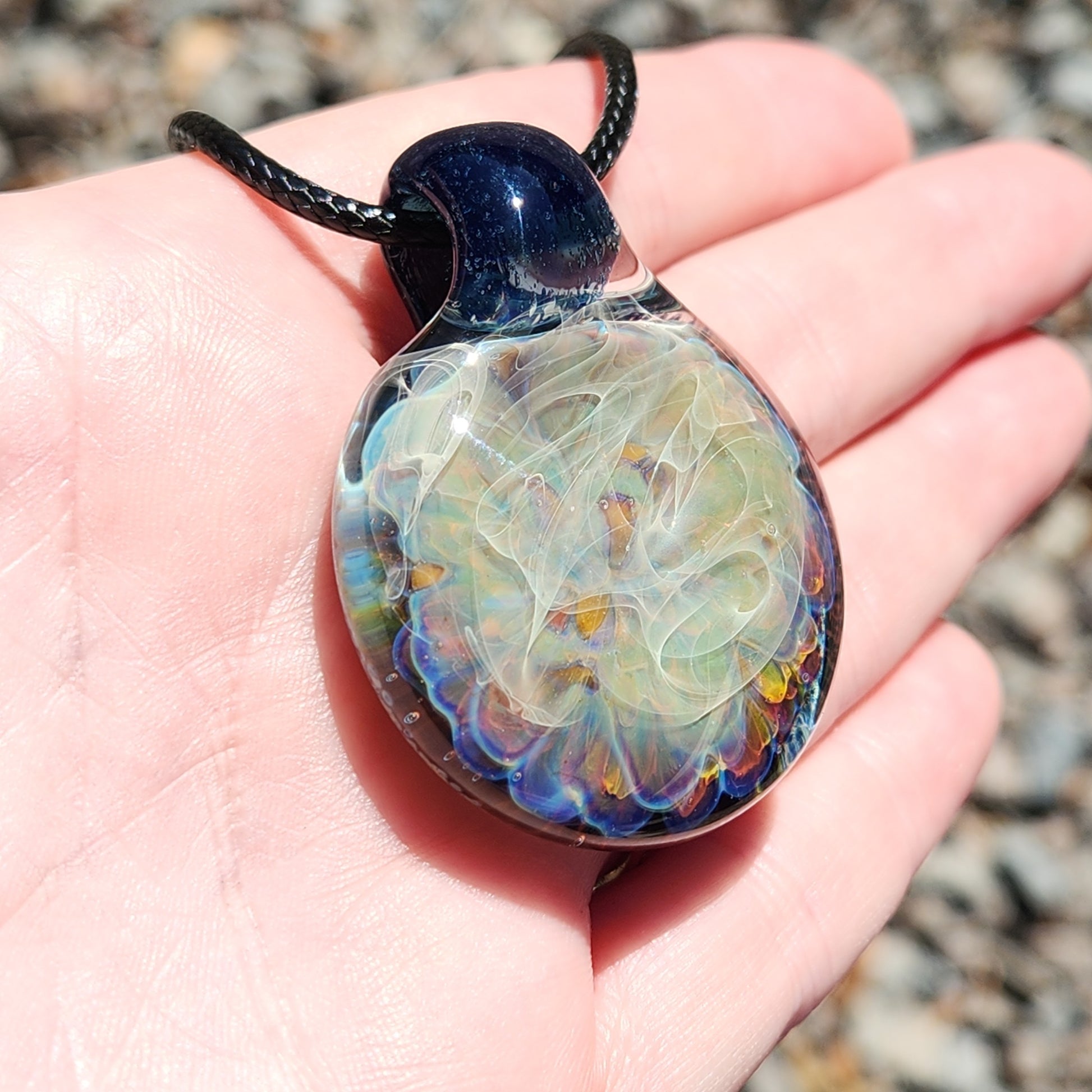 Close-up of handmade glass pendant necklace in hand, showing detailed silver fuming and vibrant borosilicate glass colors.