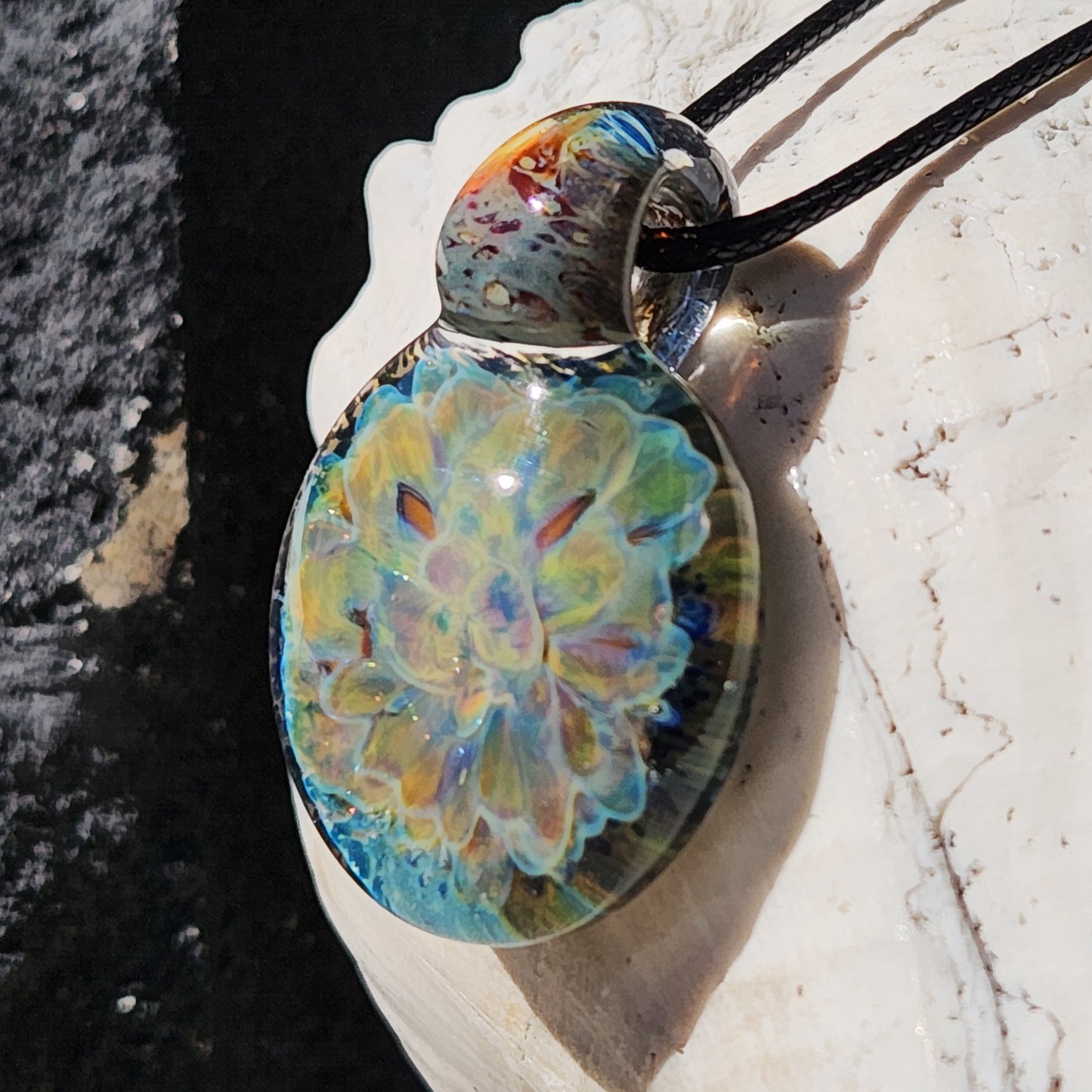 Side view of the handmade glass pendant necklace with vibrant blue and yellow flower pattern, resting on a white seashell.