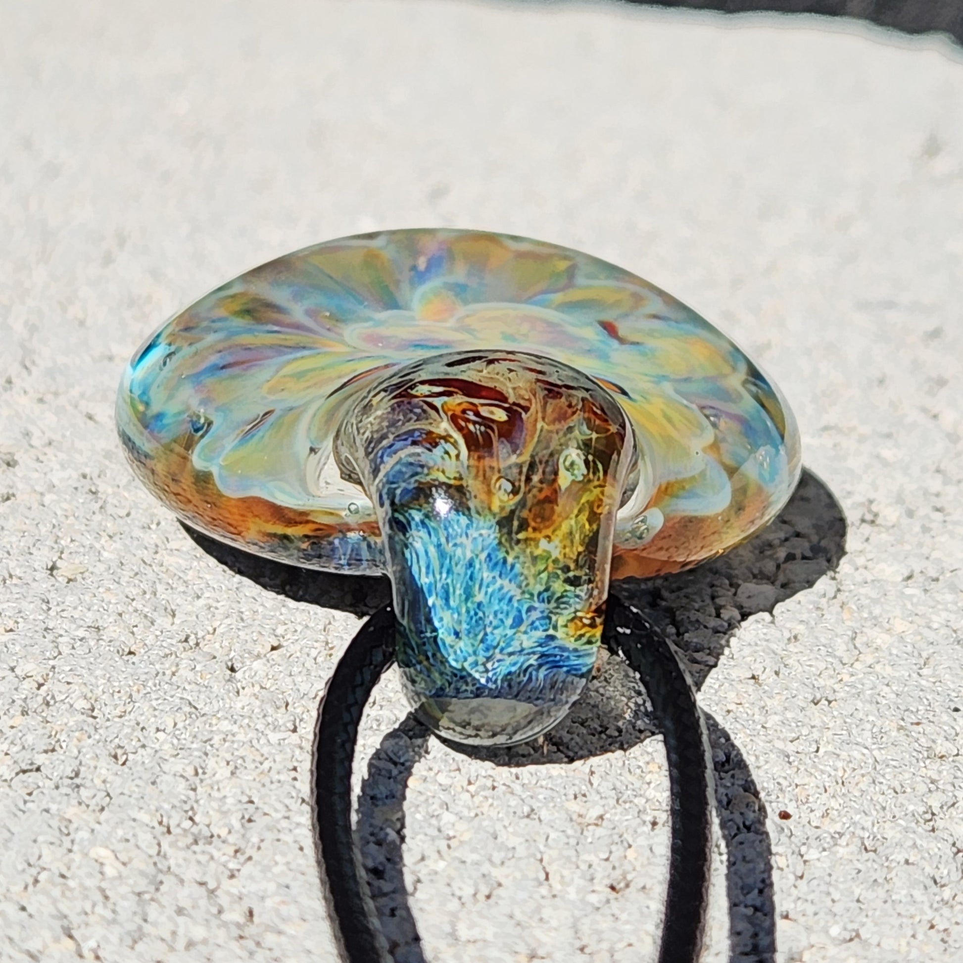 Close-up of the handmade borosilicate glass pendant showing intricate yellow-blue swirls and a textured loop for the necklace cord.