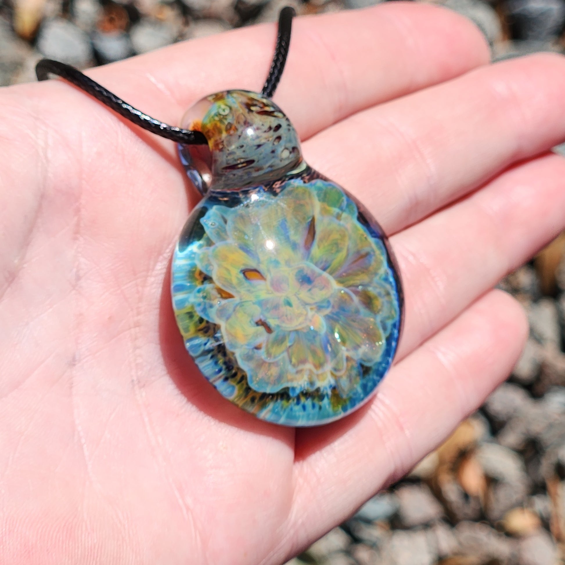 Handheld view of the handmade glass pendant necklace with a vibrant yellow and blue flower design, highlighting its size and detail.