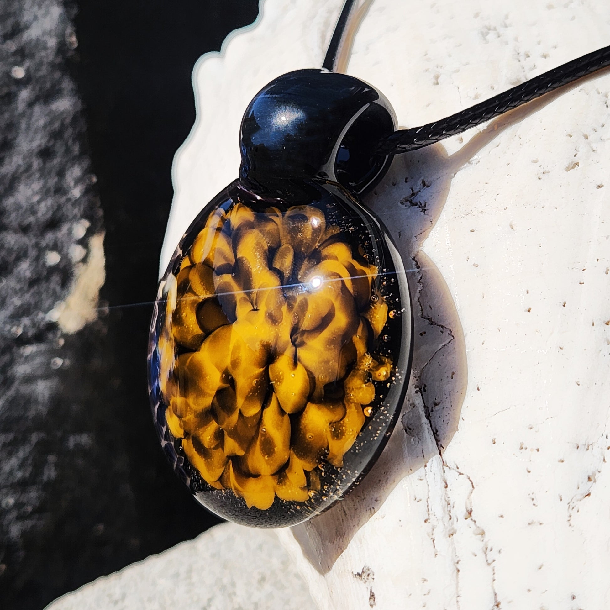 Close-up of handmade glass pendant necklace showing detailed yellow and black spiral design with glossy finish.