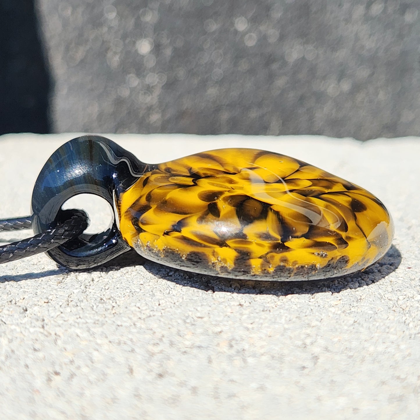 Side view of handmade glass pendant with domed yellow and black spiral design, highlighting its thickness and craftsmanship.