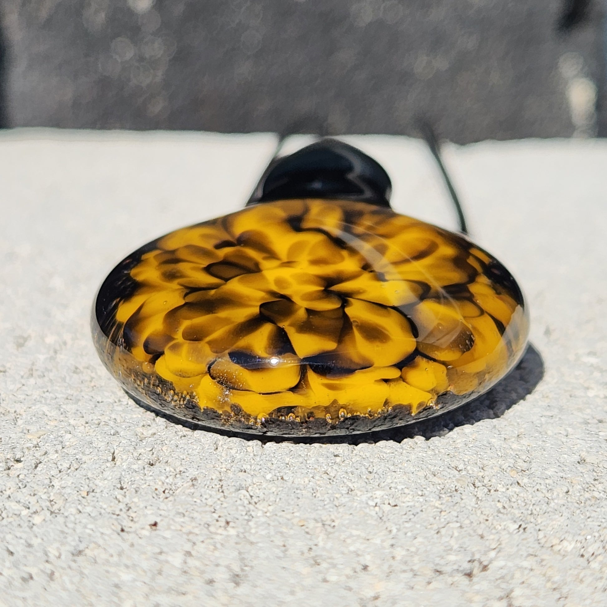 Flat-lay of handmade yellow and black spiral glass pendant showing its smooth, rounded surface and vibrant color pattern.