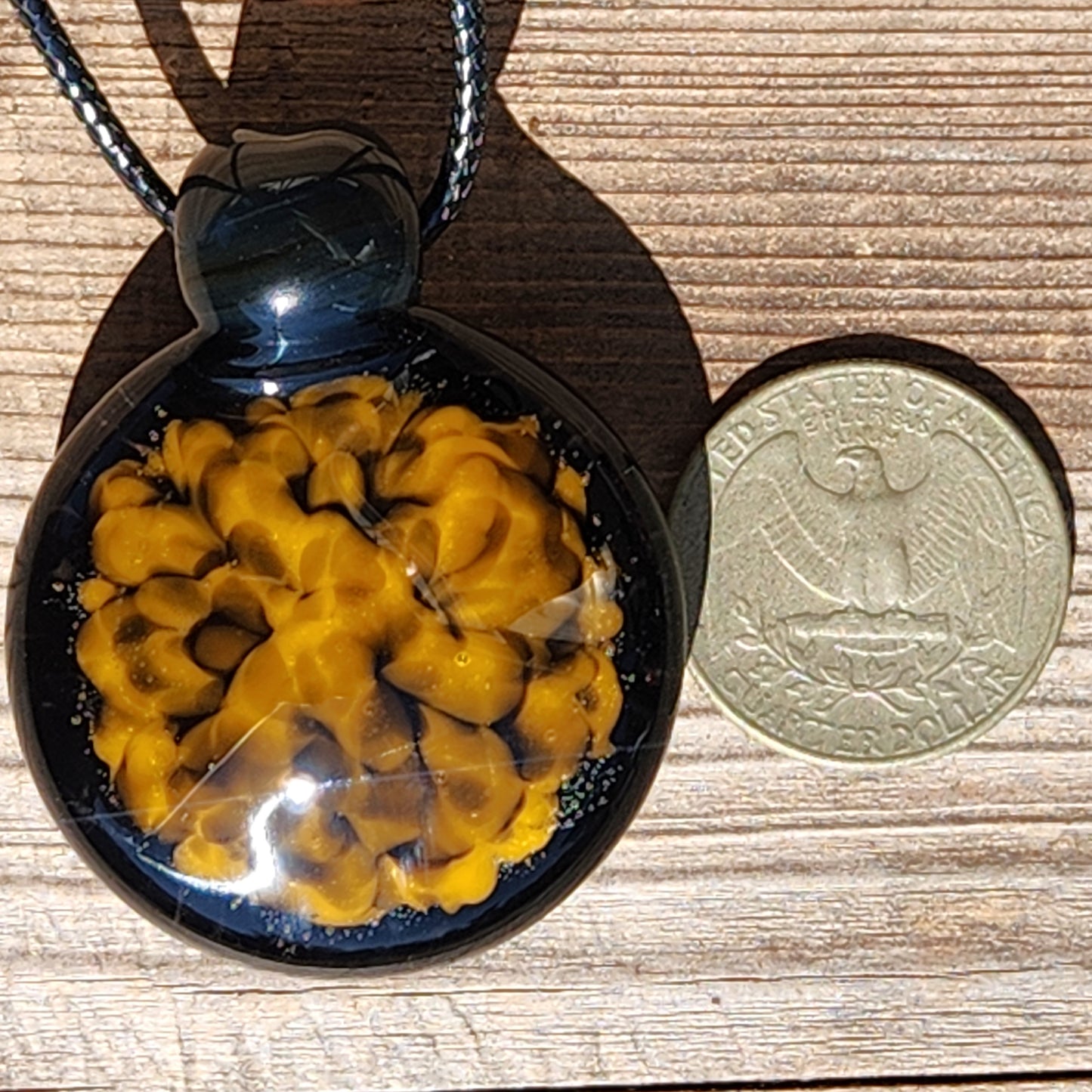 Handmade spiral glass pendant in yellow and black shown next to a US half dollar coin for size comparison.