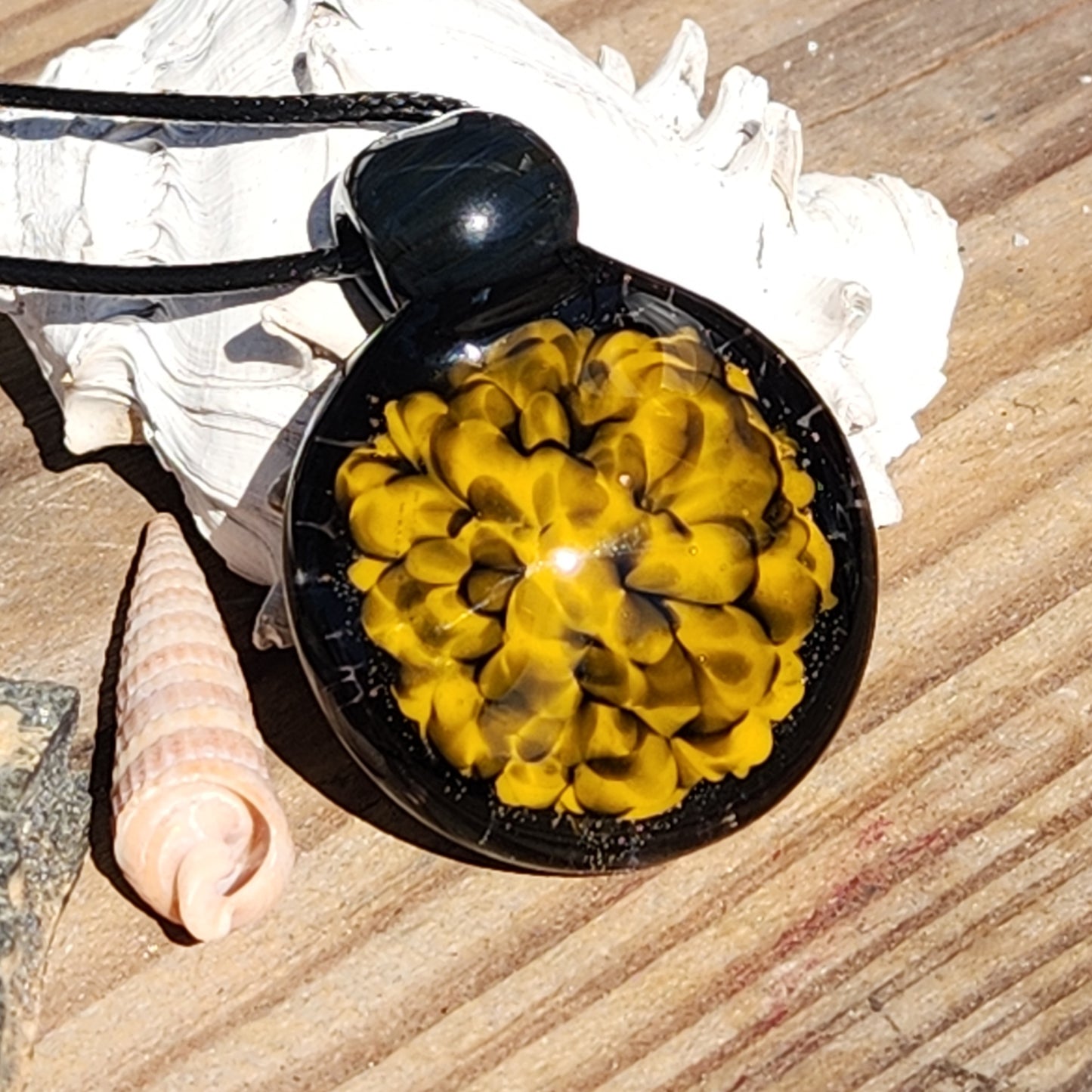 Handmade glass pendant necklace with bold yellow spiral design placed on wood with seashells, ideal for boho jewelry lovers.