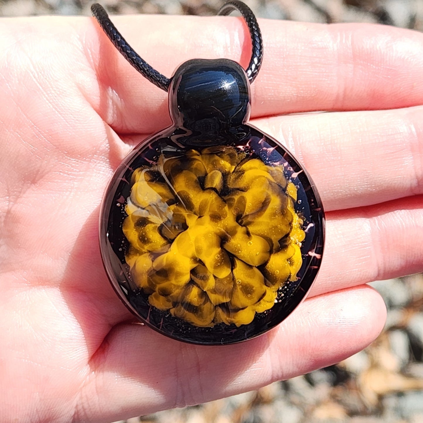 Close-up of handmade yellow and black spiral glass pendant resting in a hand, highlighting its intricate blown glass design.