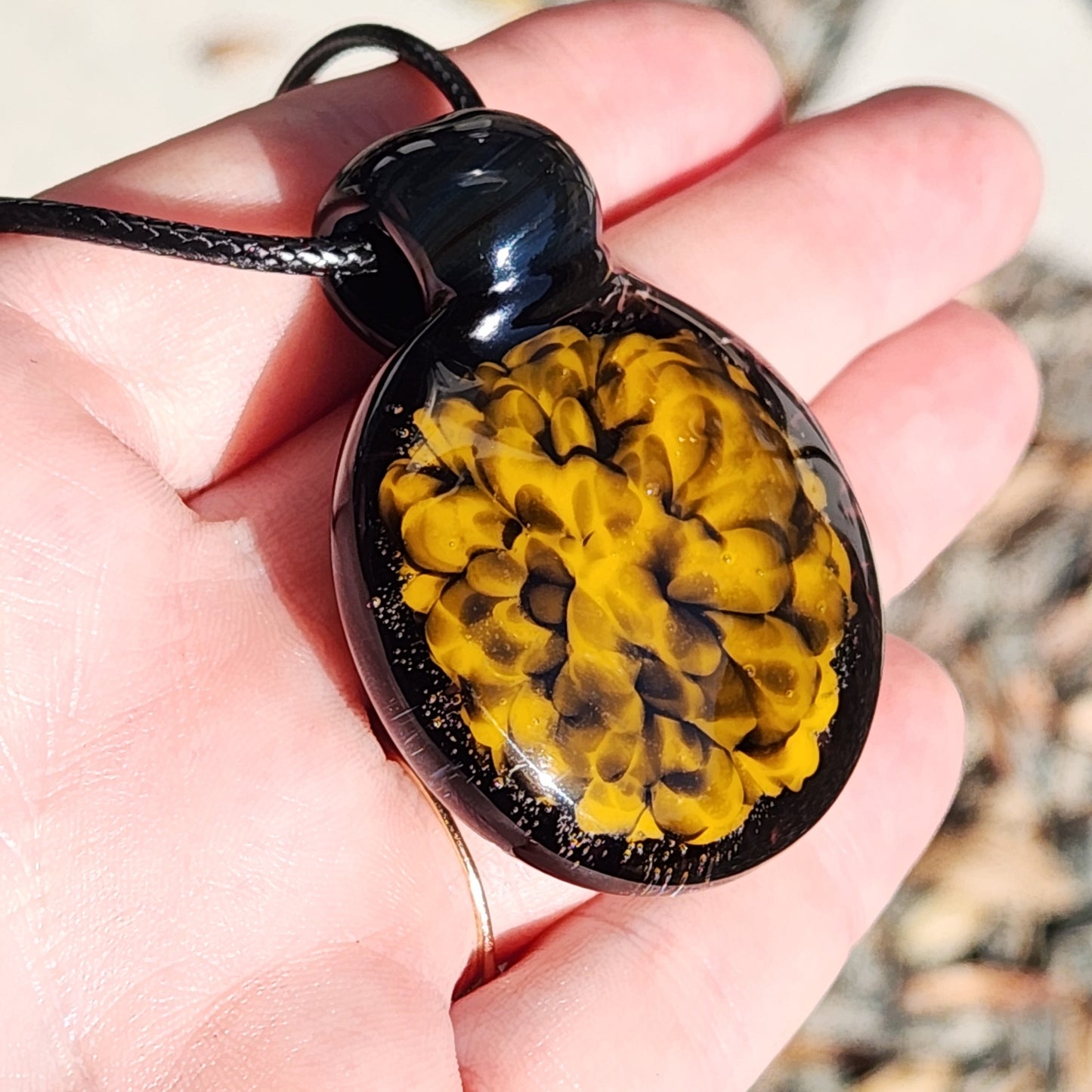 Hand holding handmade glass pendant necklace with bold yellow and black spiral design, showing wearable size and detail.