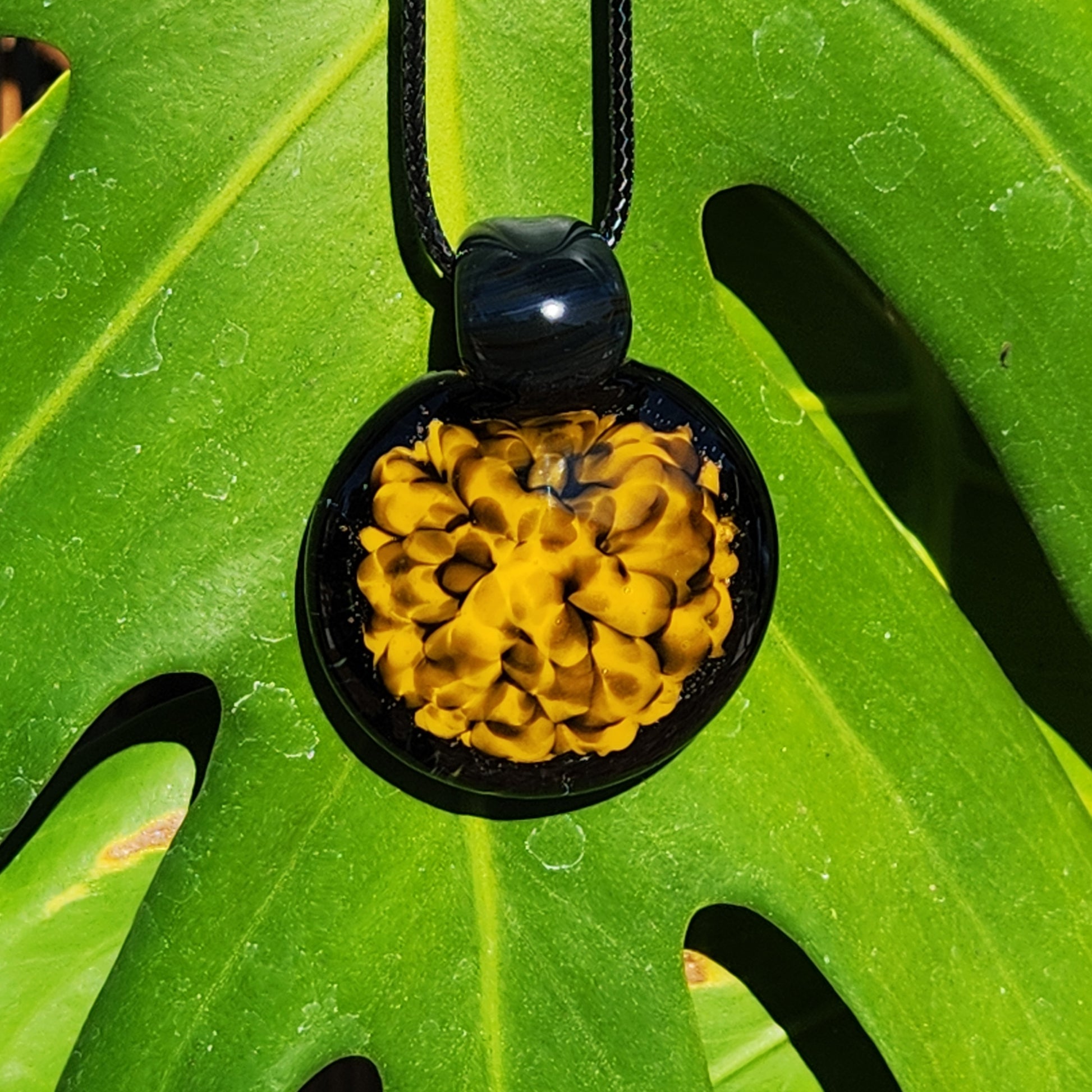 Bold spiral handmade glass pendant in yellow and black, hanging against a vibrant green leaf for natural contrast.