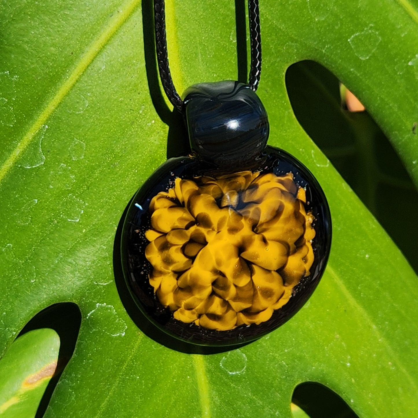 Yellow and black handmade glass pendant necklace hanging on a green leaf, emphasizing its bold spiral design and shine.