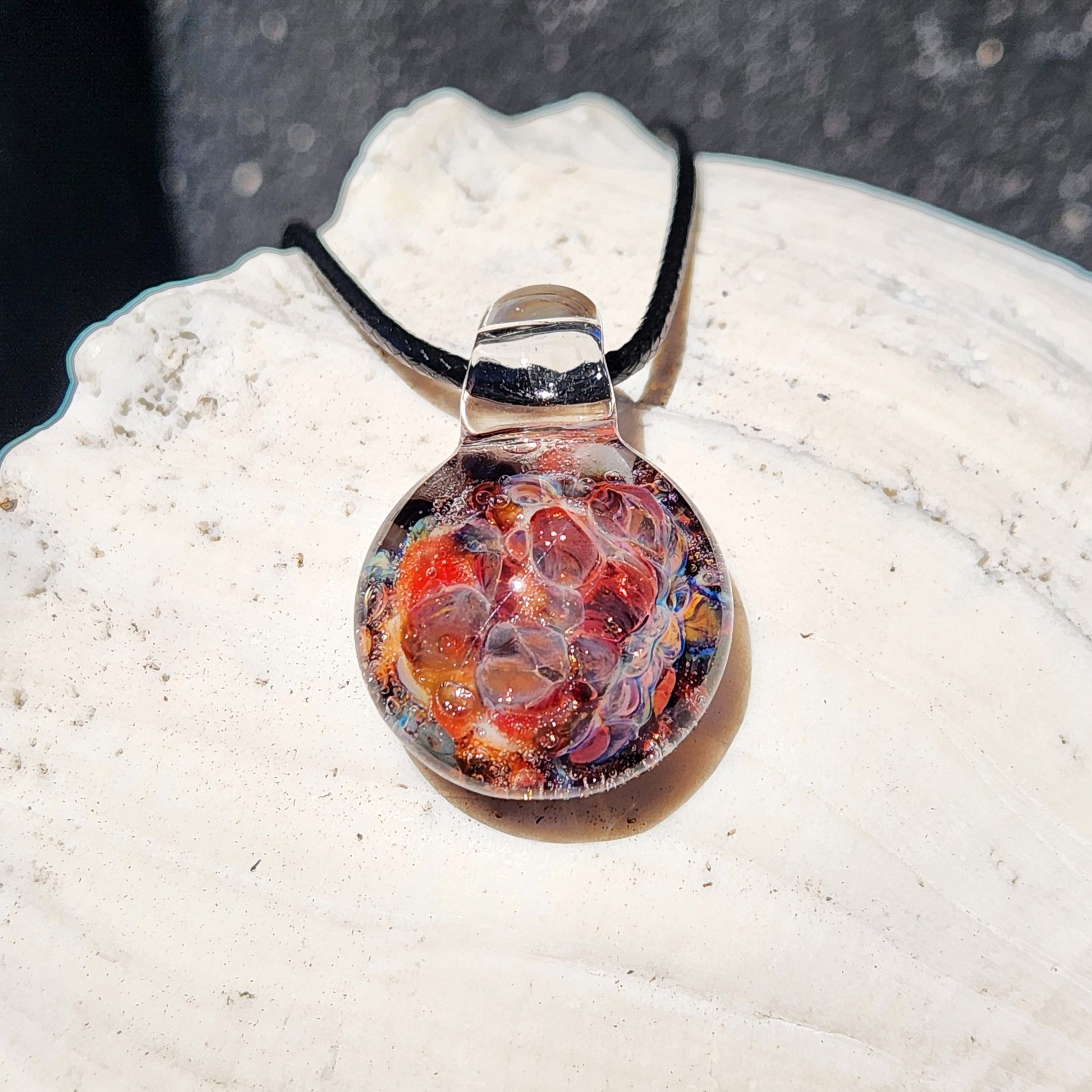 Colorful handmade glass pendant necklace resting on a white seashell, showcasing kiln-annealed bubble glass texture.