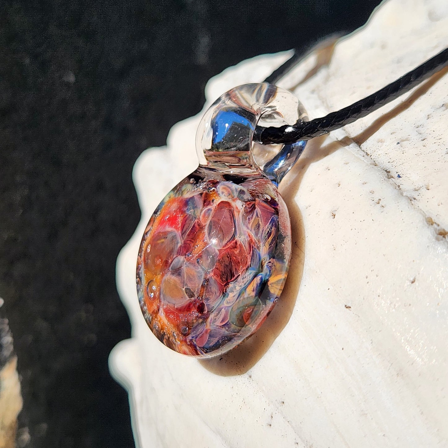 Close-up side view of borosilicate glass pendant with red and purple hues, highlighting its glossy, domed surface.