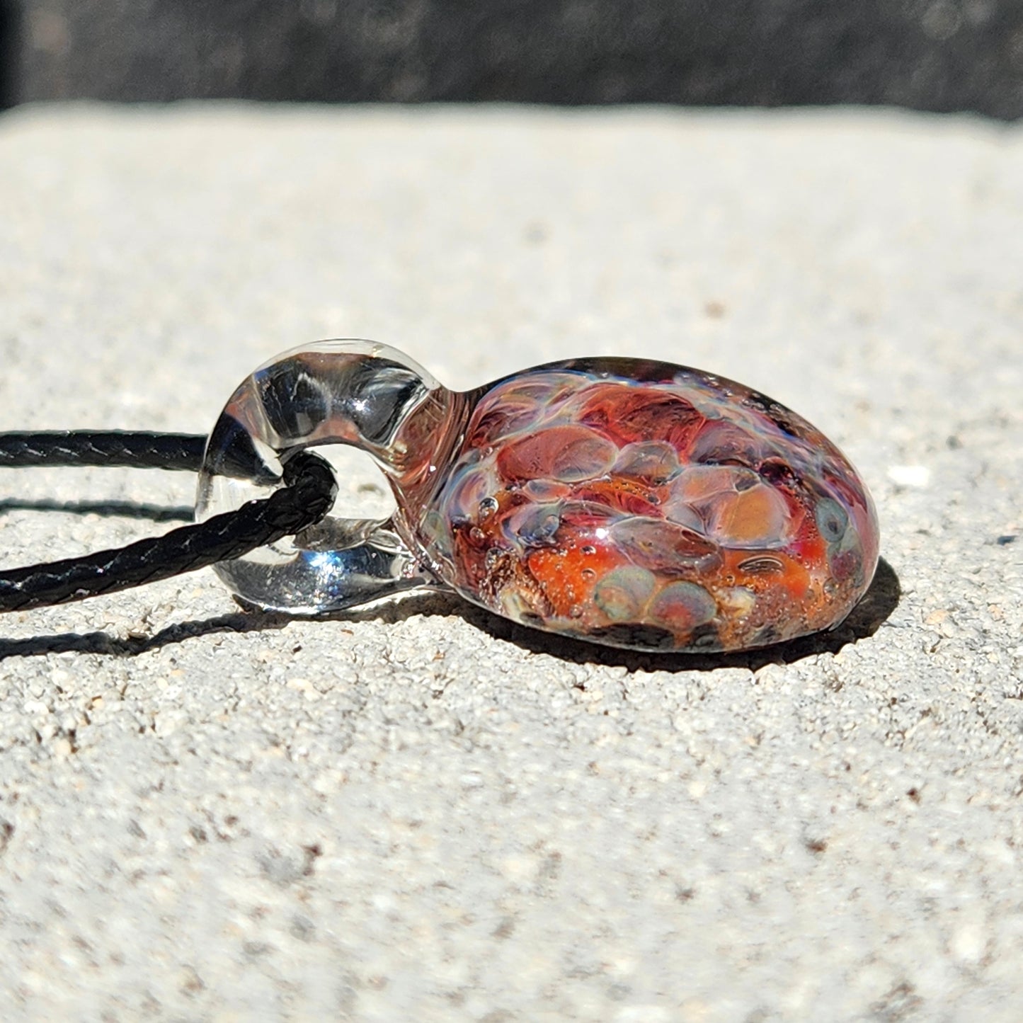 Flat-lay of bubble glass pendant necklace on concrete, showing its compact size and colorful interior design.