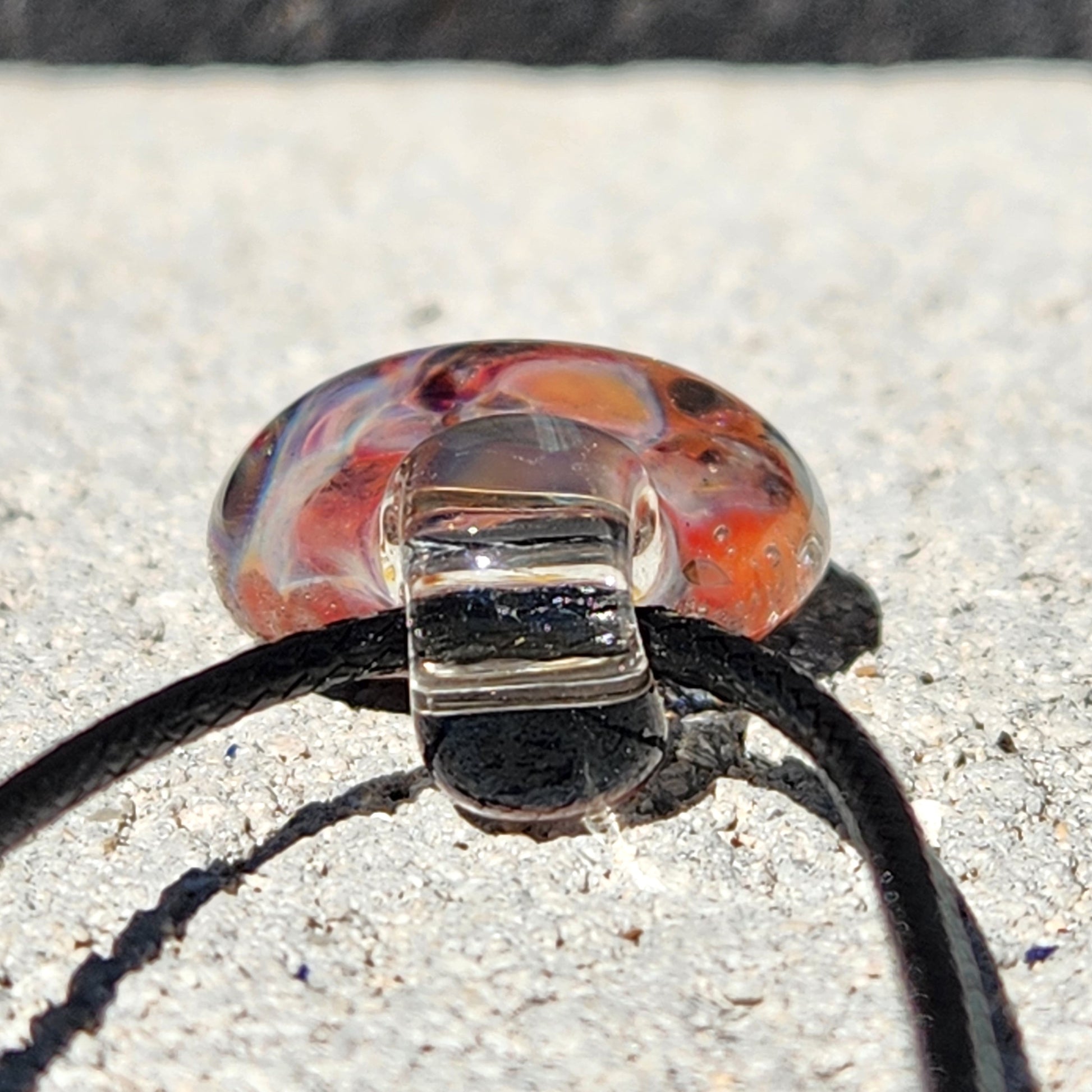 Close-up of pendant loop and cord attachment, showing clear glass top and colorful bubble glass body on stone surface.