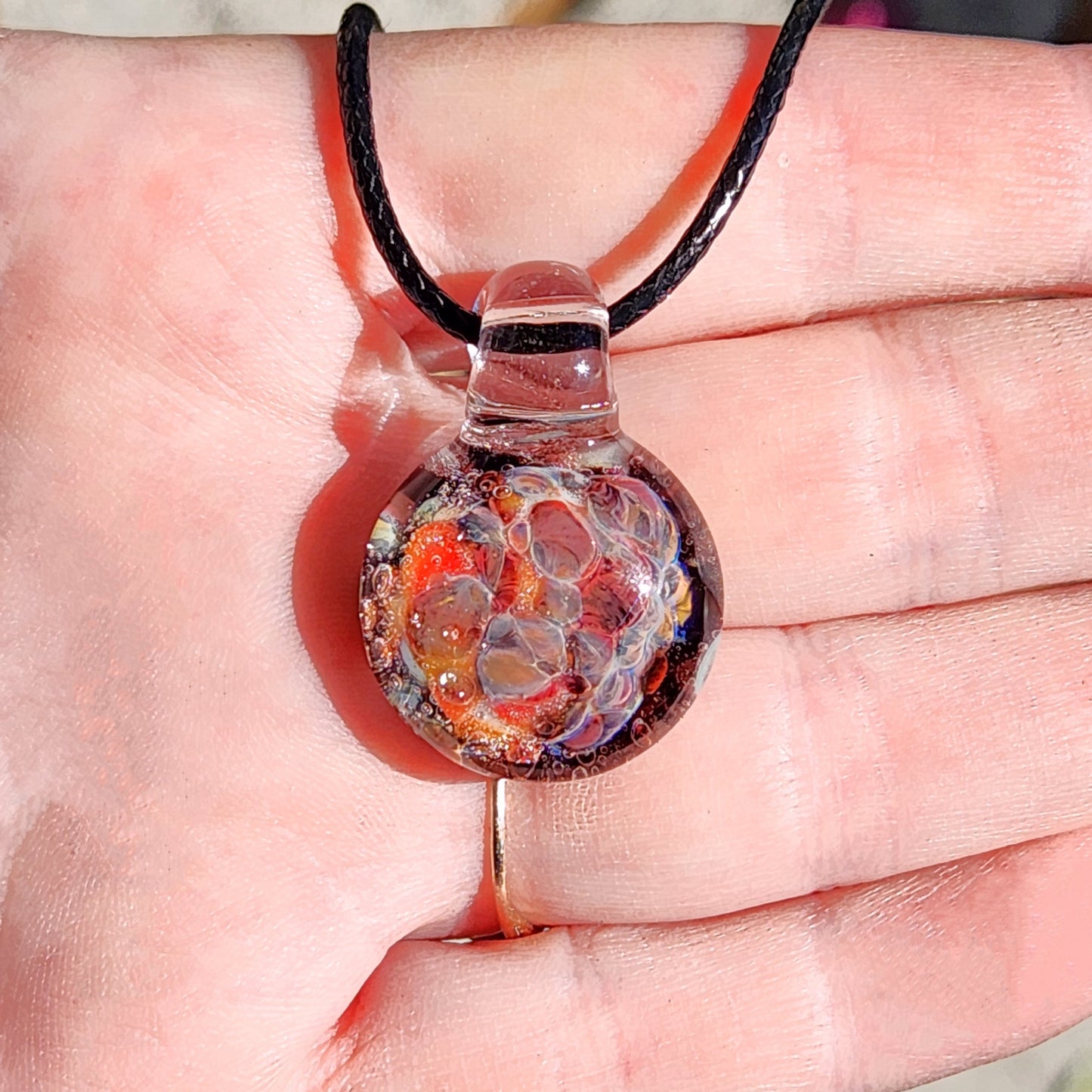 Hand holding handmade glass pendant necklace, showing its small size and vibrant red bubble glass design.