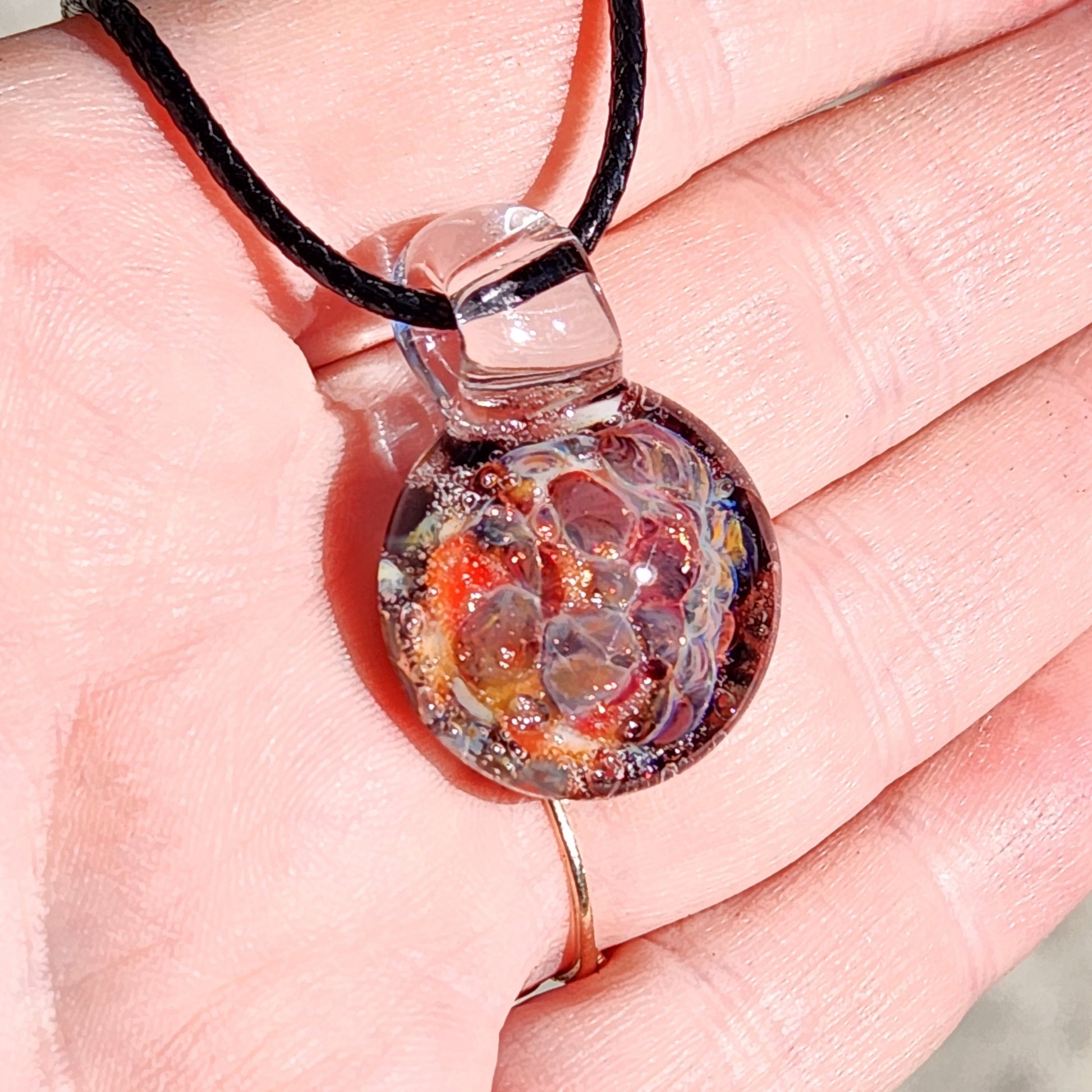 Close-up of pendant in hand, highlighting the detailed red and multicolor crushed glass pattern in borosilicate glass.