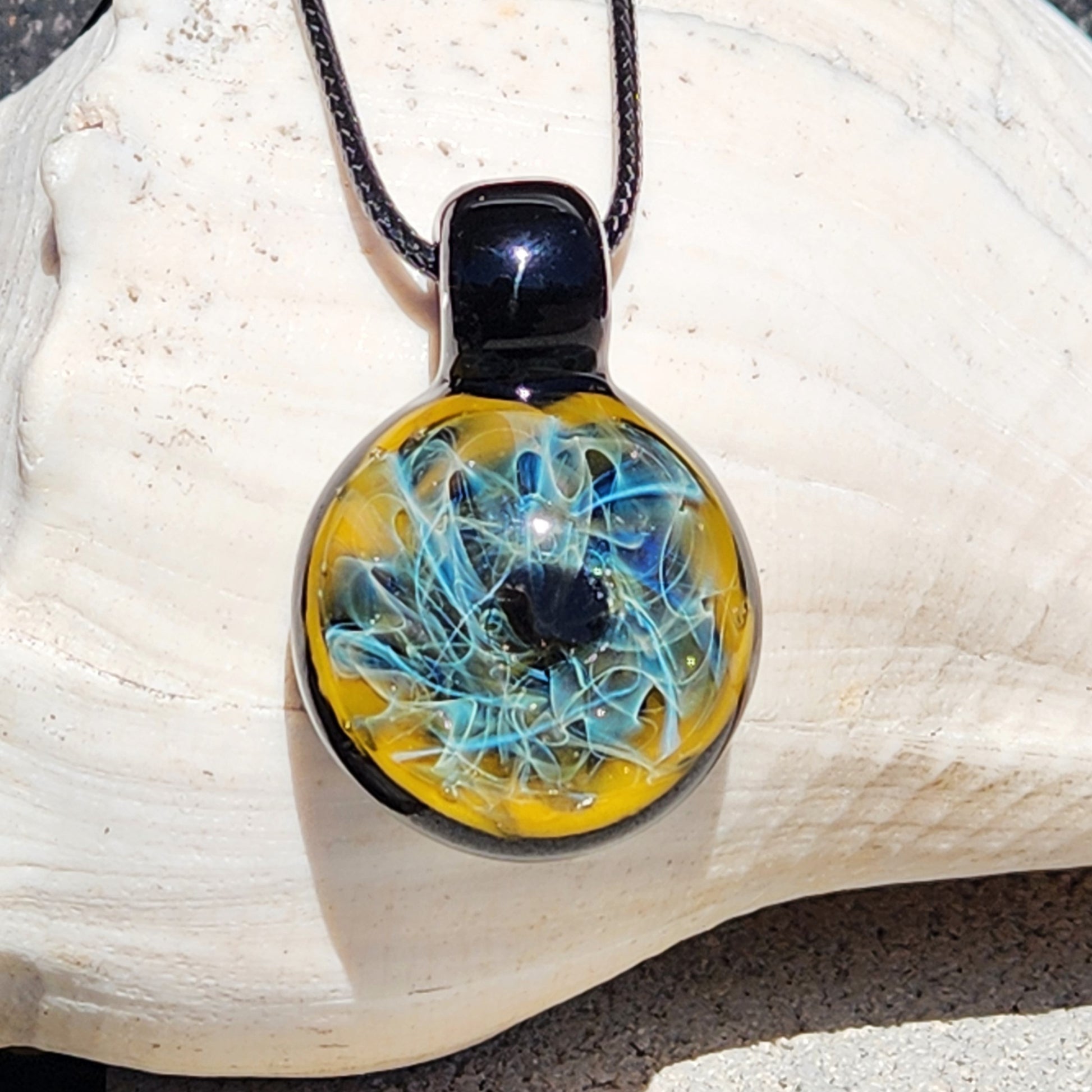 Trippy handmade glass pendant necklace with swirling blue and gold design, shown resting on a large white seashell.