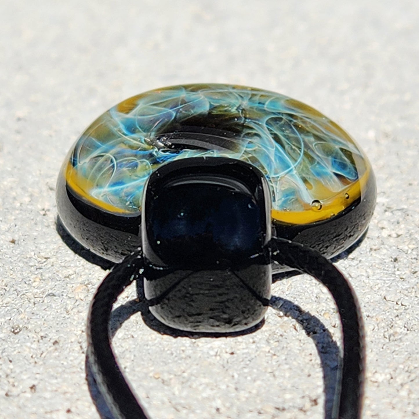 Bottom view of handmade heady glass pendant showing depth of blue and gold fumed design with black glass loop and cord.