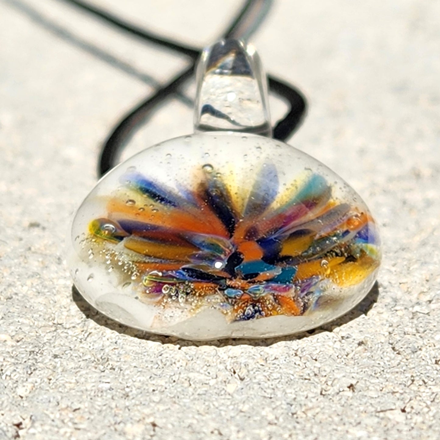Close-up of handmade rainbow flower glass pendant with white base, showcasing vibrant colors and clear glass loop. Artistic boho accessory.