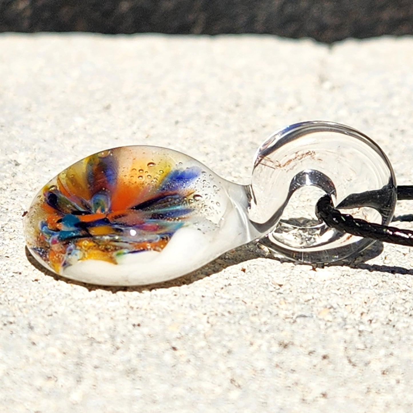 Side view of handmade borosilicate glass pendant with colorful flower design, highlighting its clear loop and domed shape. Boho charm necklace.