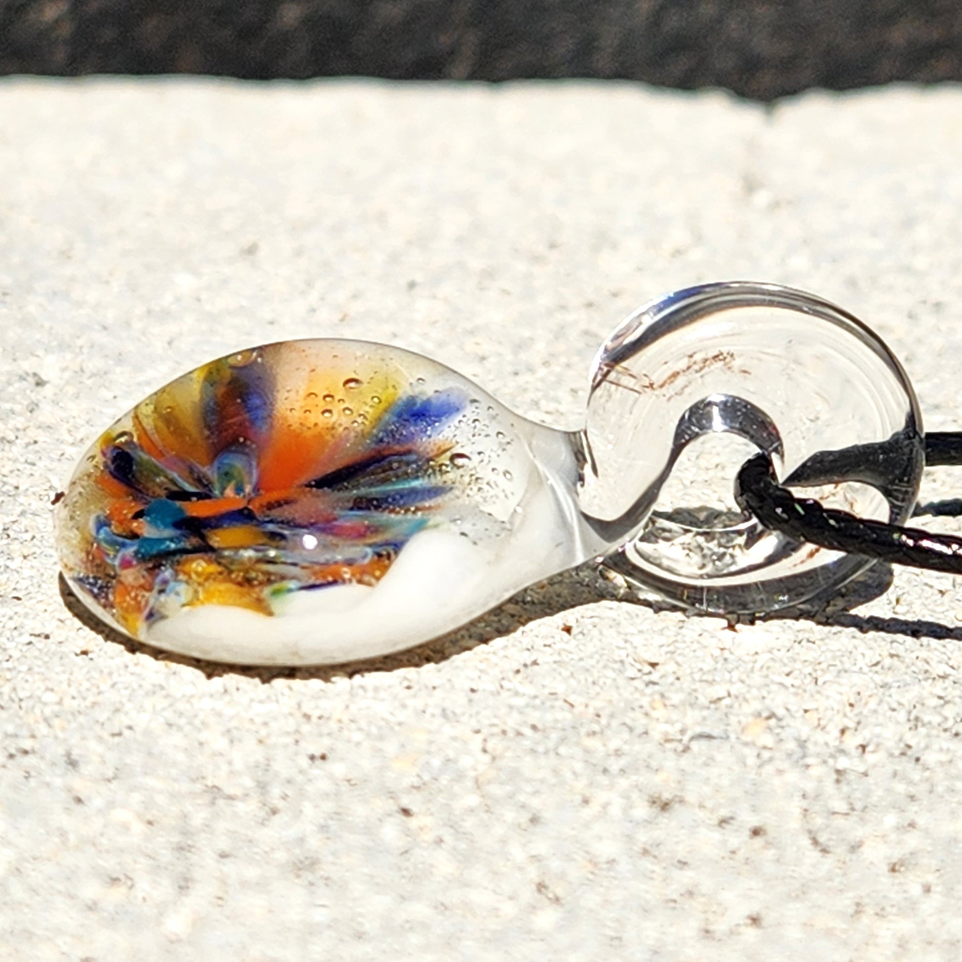 Side view of handmade borosilicate glass pendant with colorful flower design, highlighting its clear loop and domed shape. Boho charm necklace.